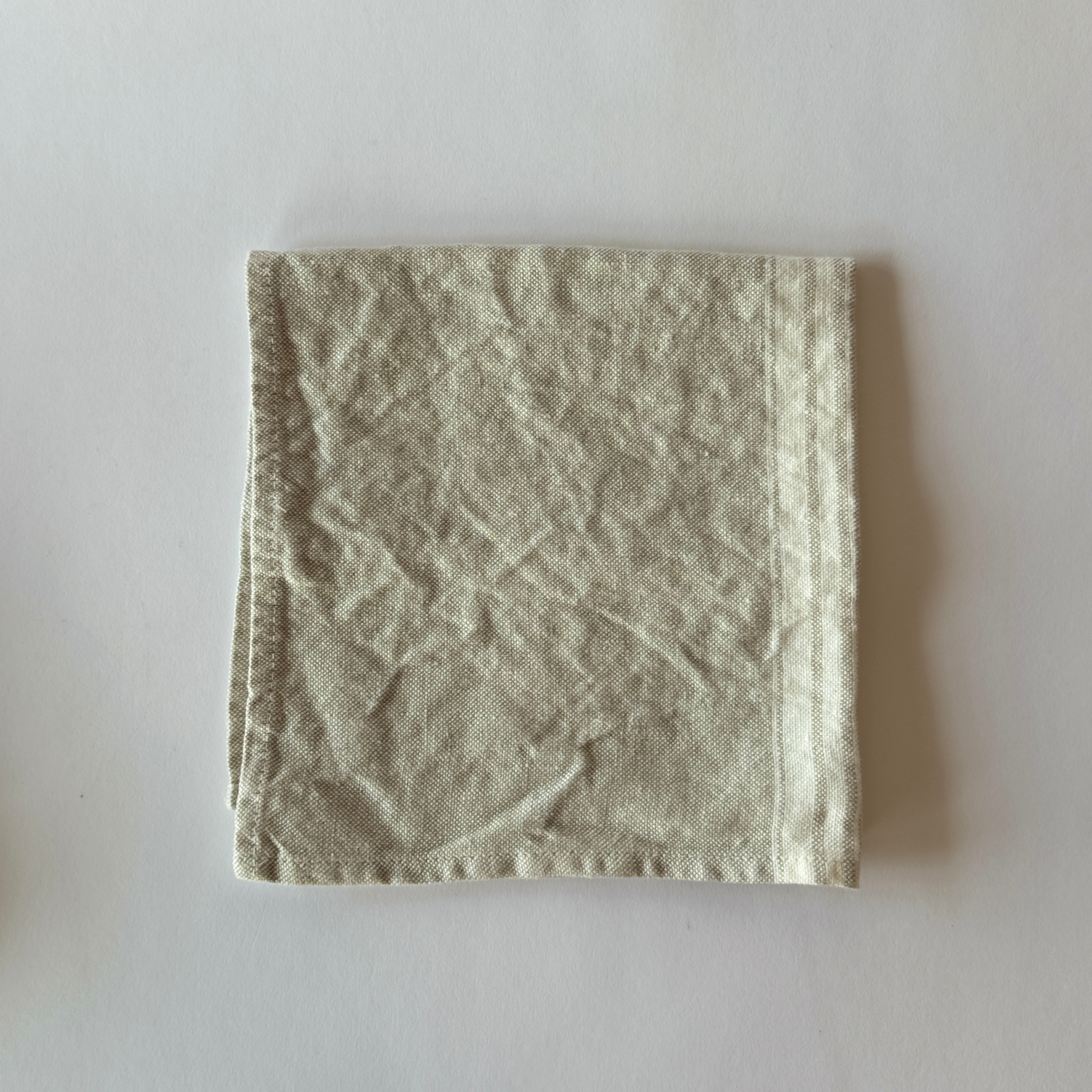 A folded light gray Maison Table Napkin by Grace & Company on a white surface.