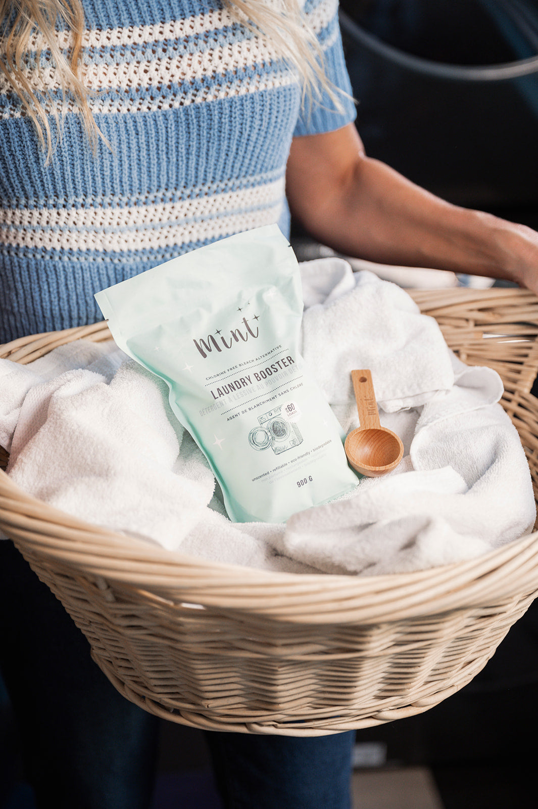 Person holding a laundry basket with white towels, wooden scoop, and Grace & Company Mint Cleaning Products.