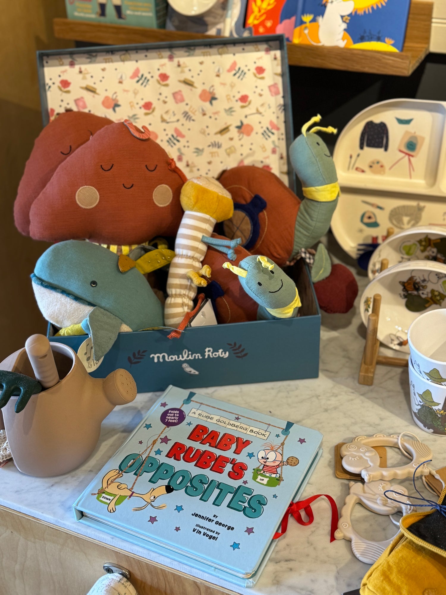 Box of plush toys, a book titled Baby Rubys Opposites, and various kids items displayed on a table.