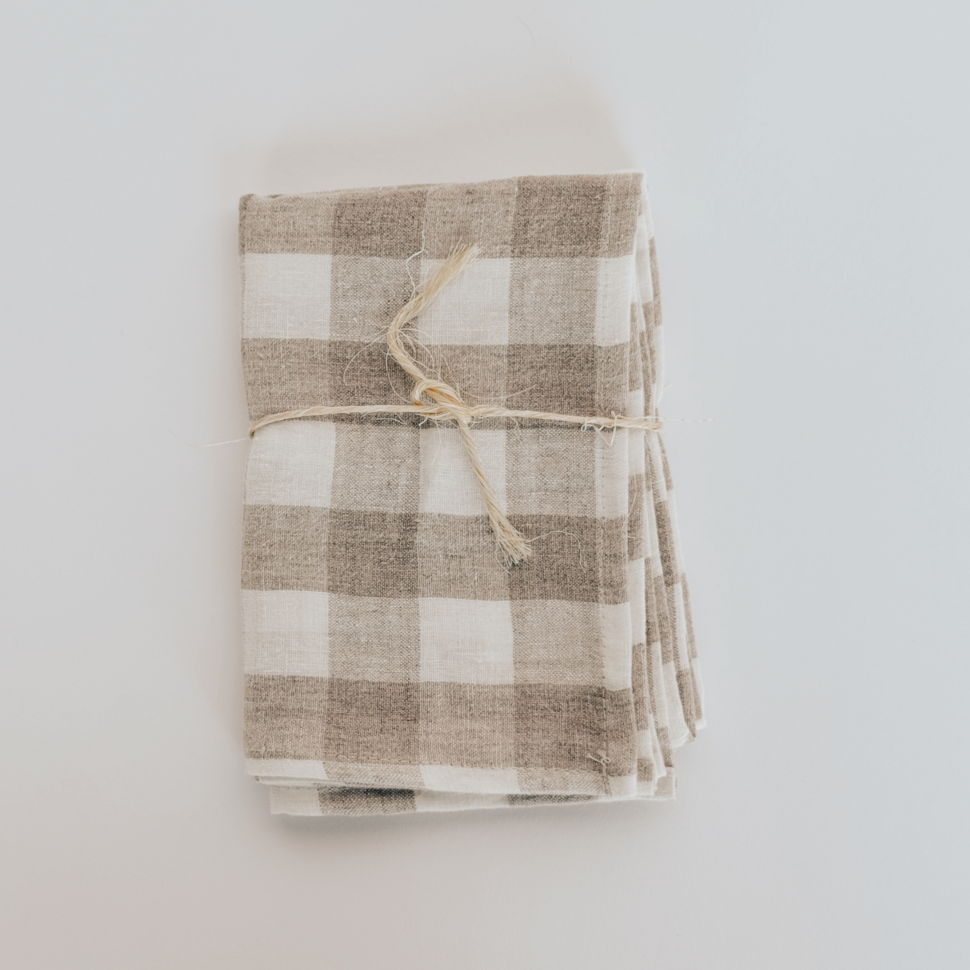 The Linen Way Kitchen Cloth Tuile by Grace & Company, folded and tied with twine, rests on a white surface.