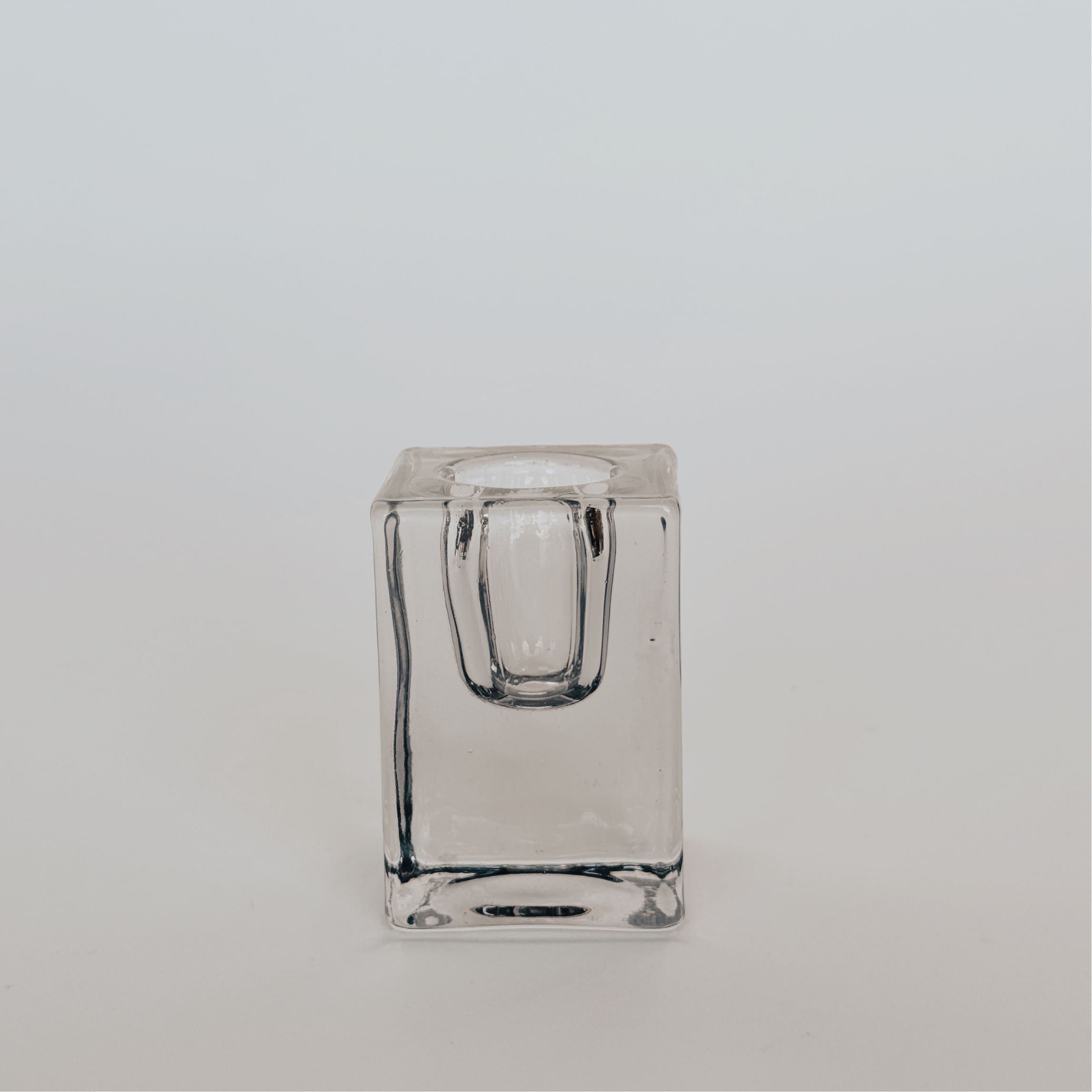 The Classic Taper Holder in black glass by Grace & Company ltd sits on a white surface, backed by a light background.