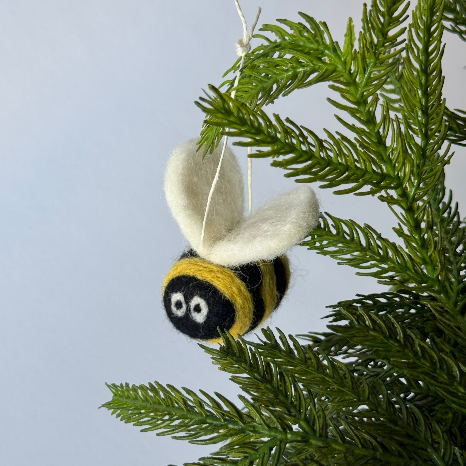 The Giant Bumble Bee Ornament by Grace & Company hangs from a green pine branch against a plain background.