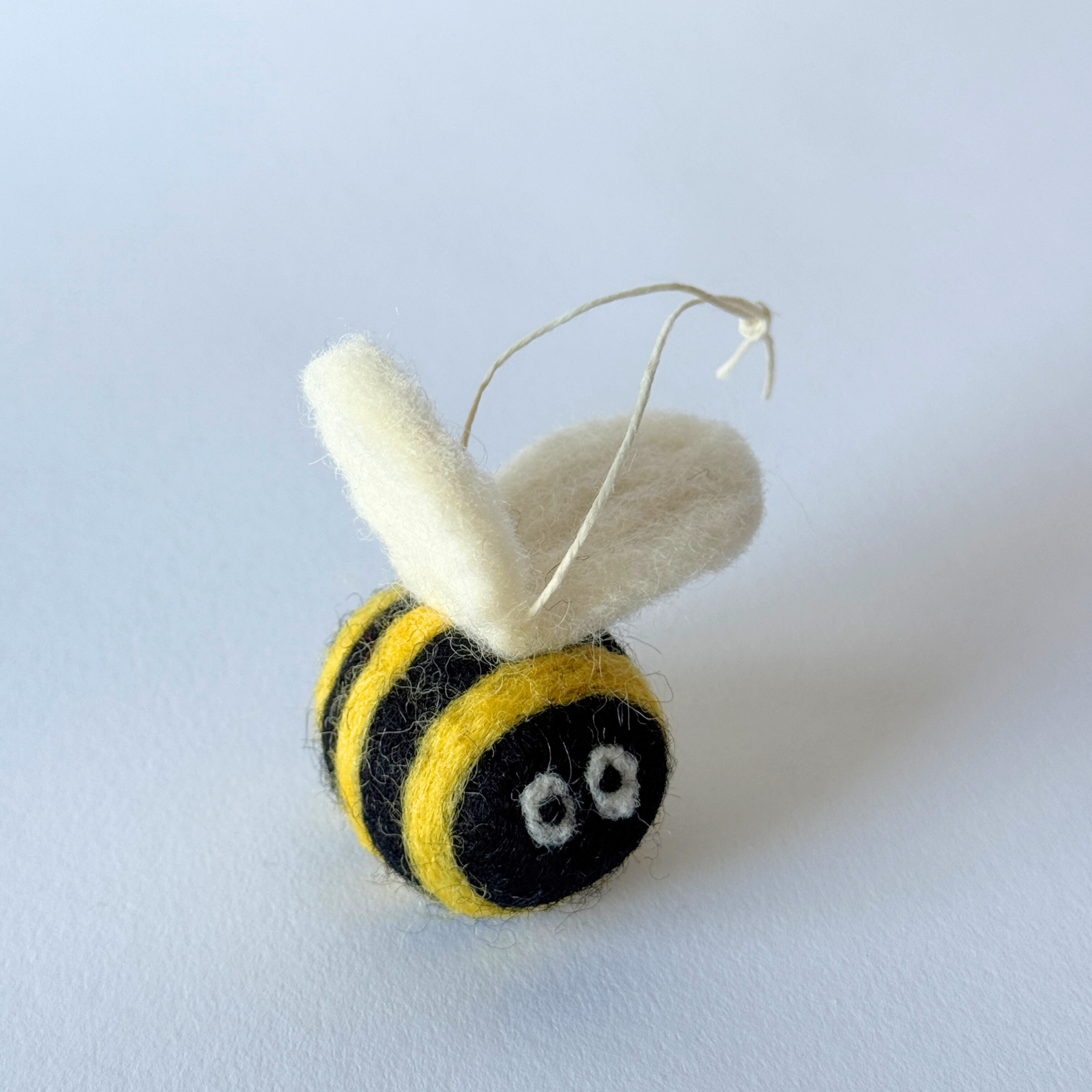 The Giant Bumble Bee Ornament by Grace & Company features white wings and a string, set on a plain light background.