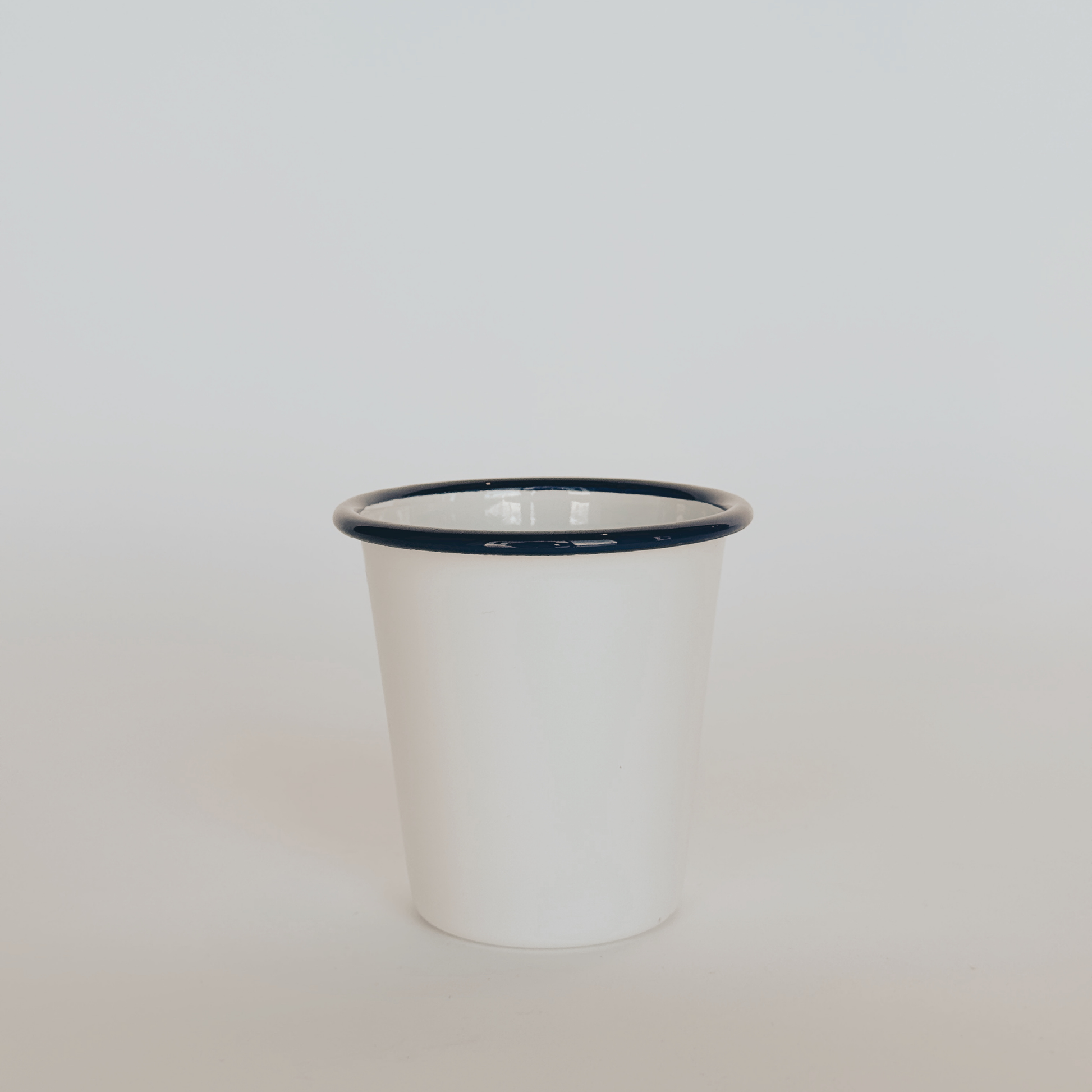 A Falcon Enamelware Tumbler by Grace & Company with a dark rim, set on a light surface against a neutral background.