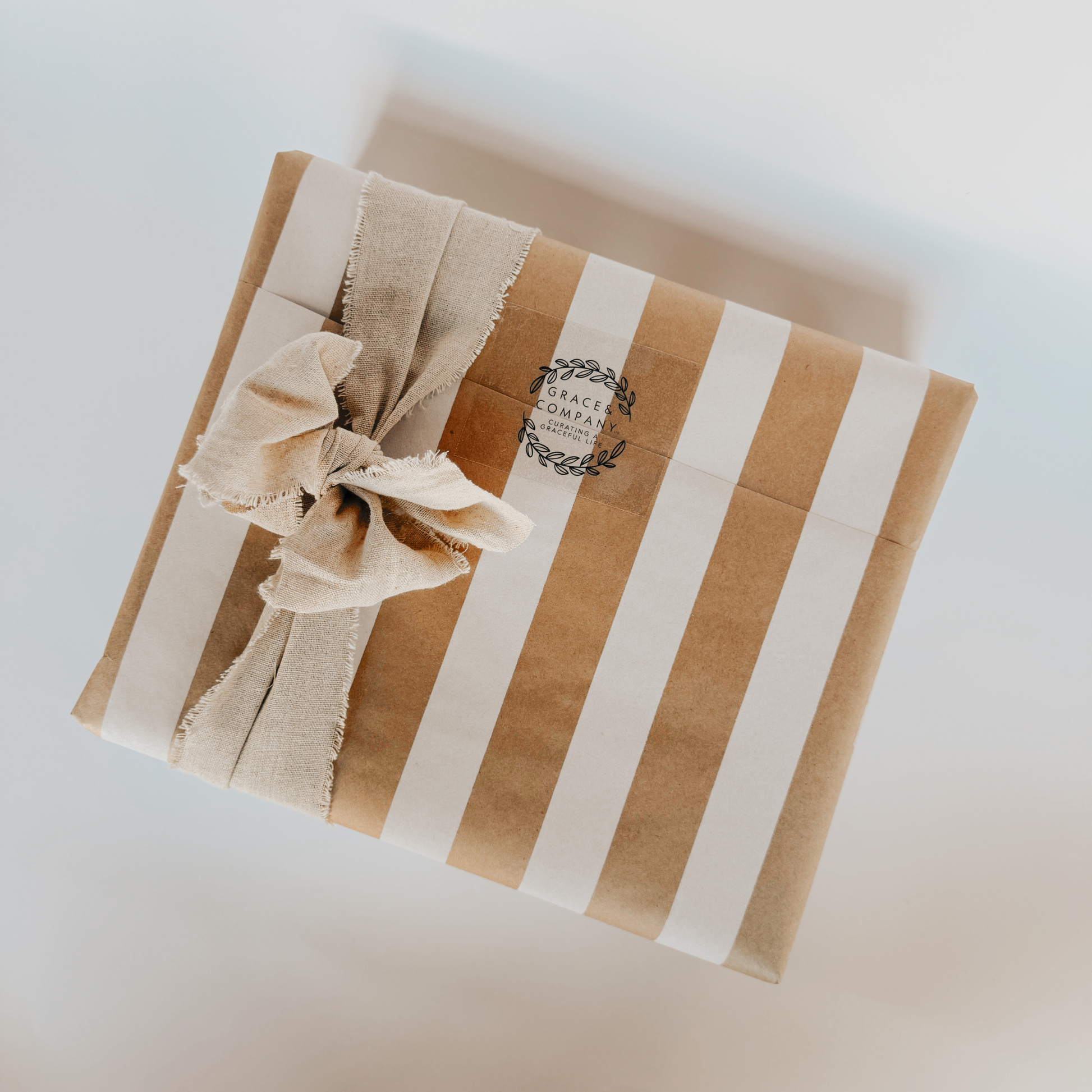 Grace & Company Gift Wrapping: brown and white stripes, beige fabric bow, and round stamped label on top.