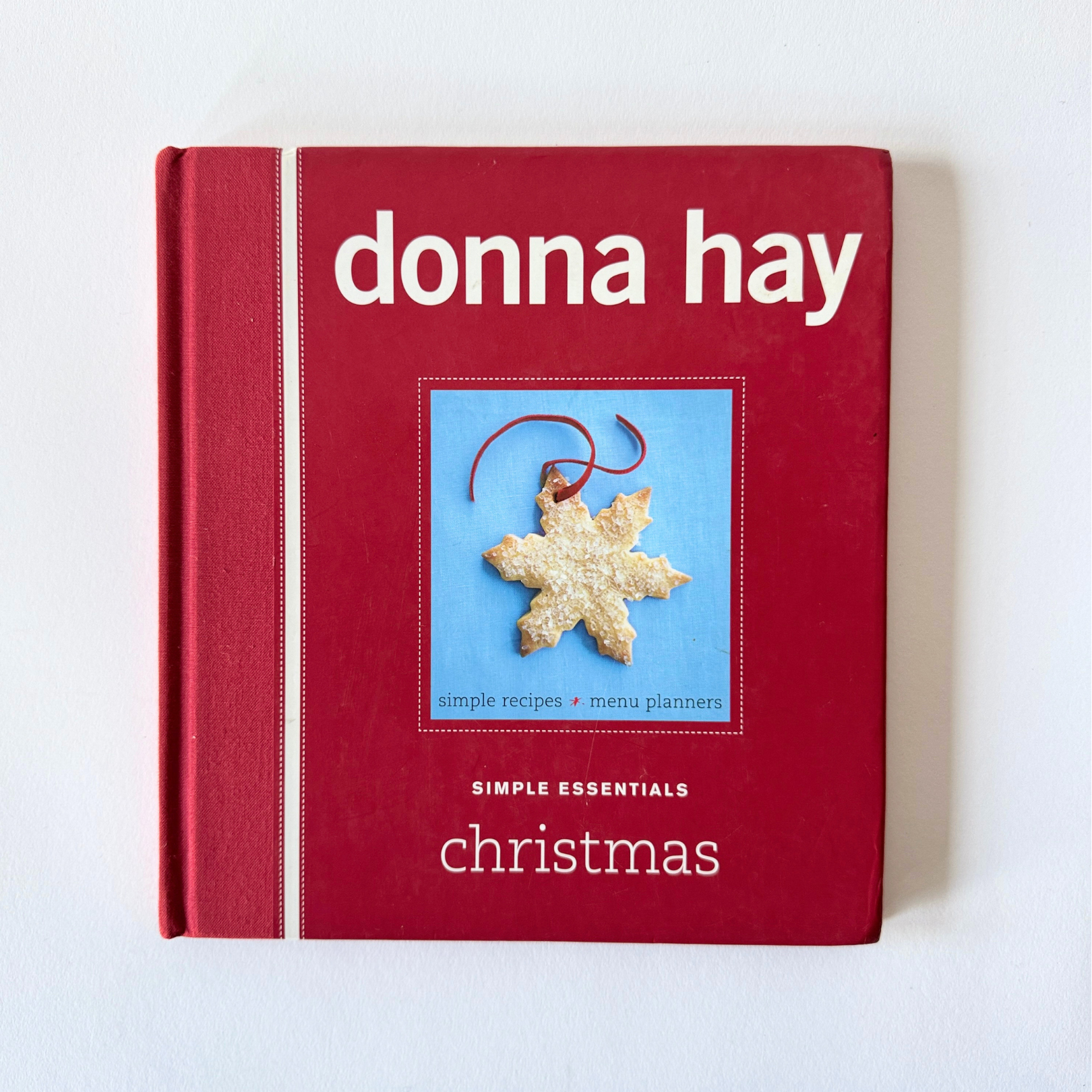 A red cookbook, Donna Hay Simple Essential Christmas - Vintage by Grace & Company, with a snowflake cookie on the cover.