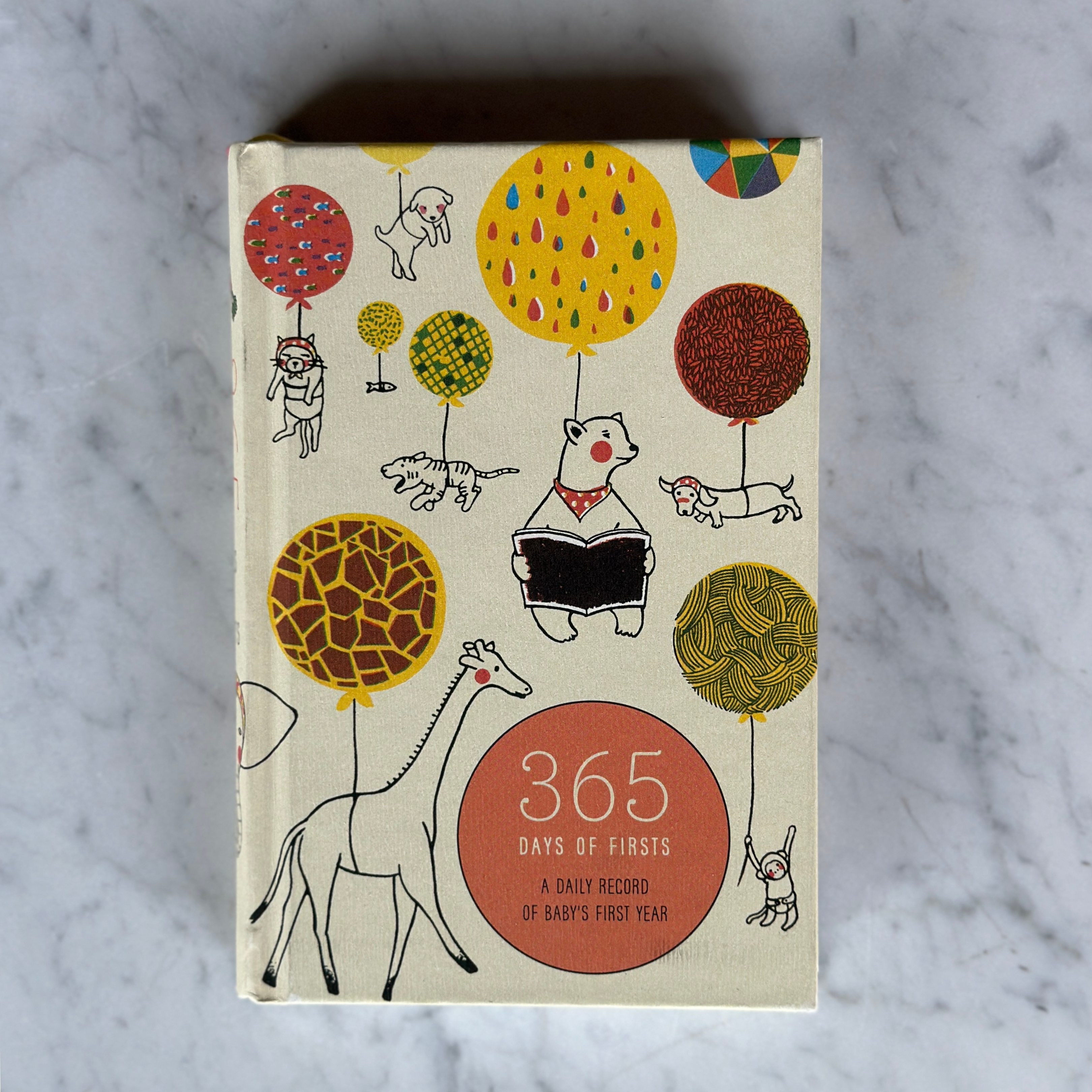 Grace & Company’s 365 Days of Firsts journal features animals with colorful balloons on a marble background.