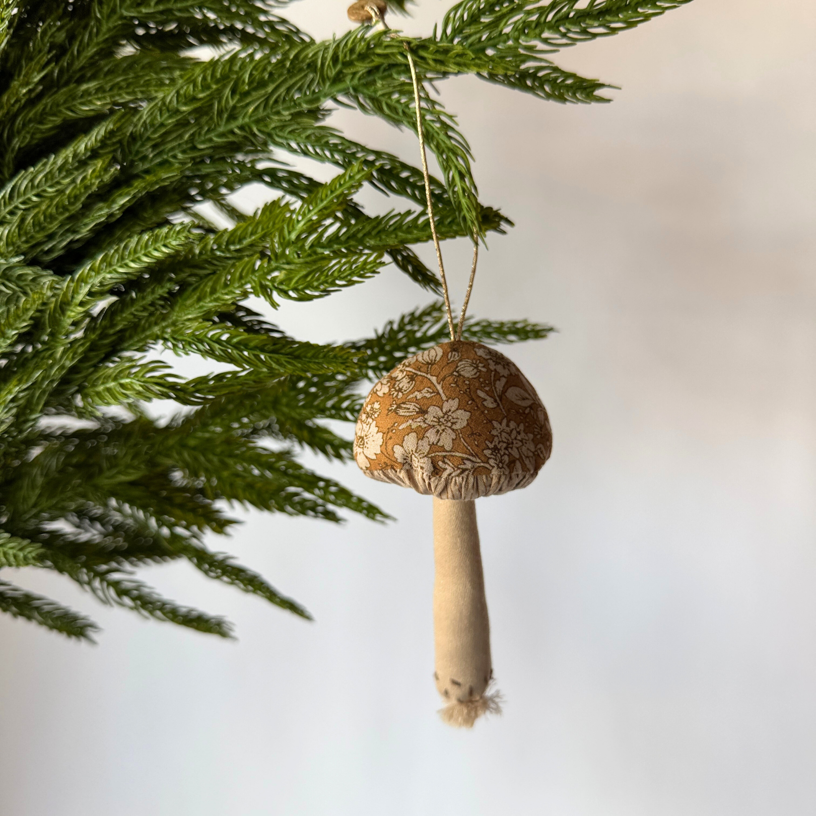 The Maileg - Mushroom Ornament by Grace & Company hangs from a pine branch, featuring a floral-patterned fabric cap.