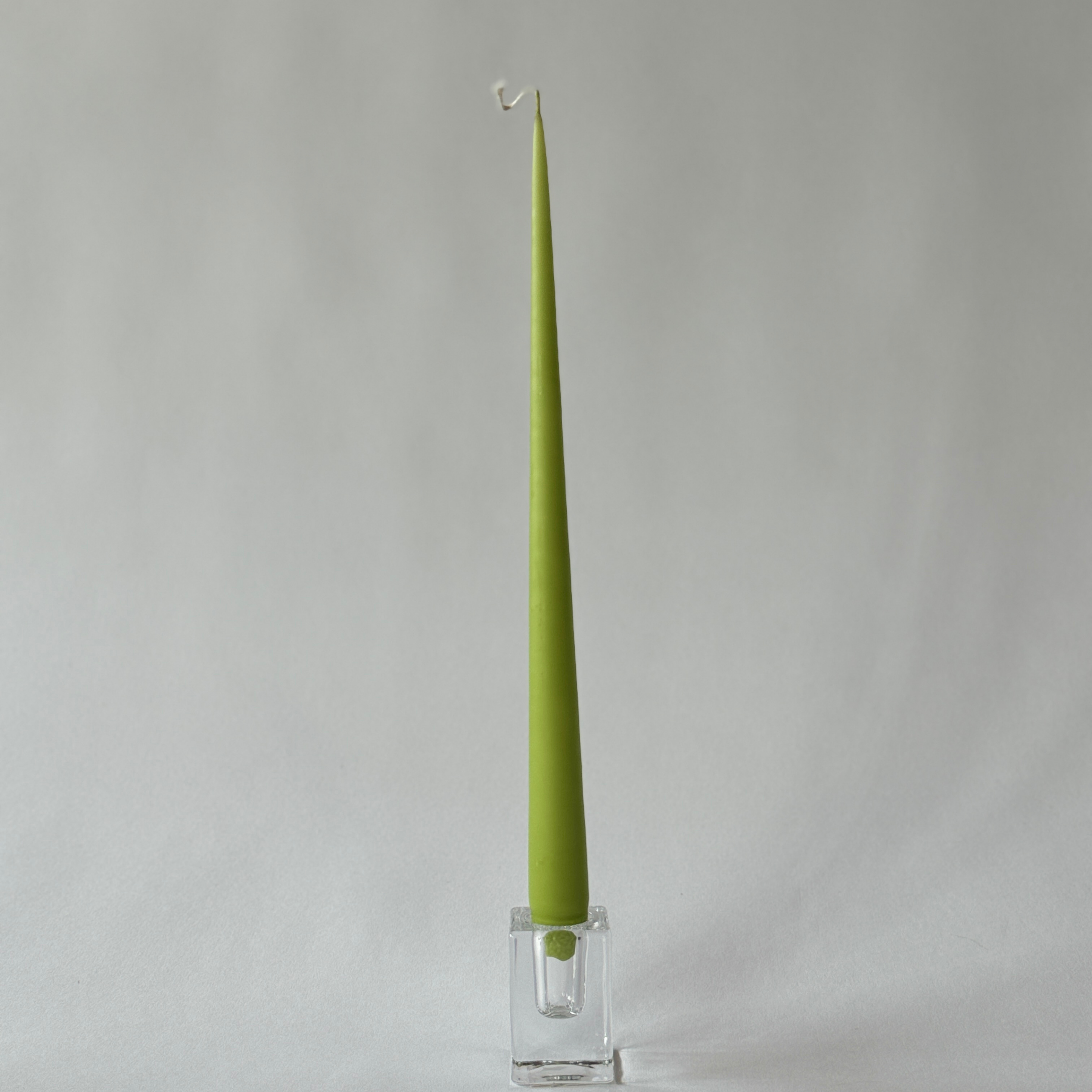 The Ester & Erik 13 green taper candle by Grace & Company ltd stands upright in a clear holder on a light gray background.