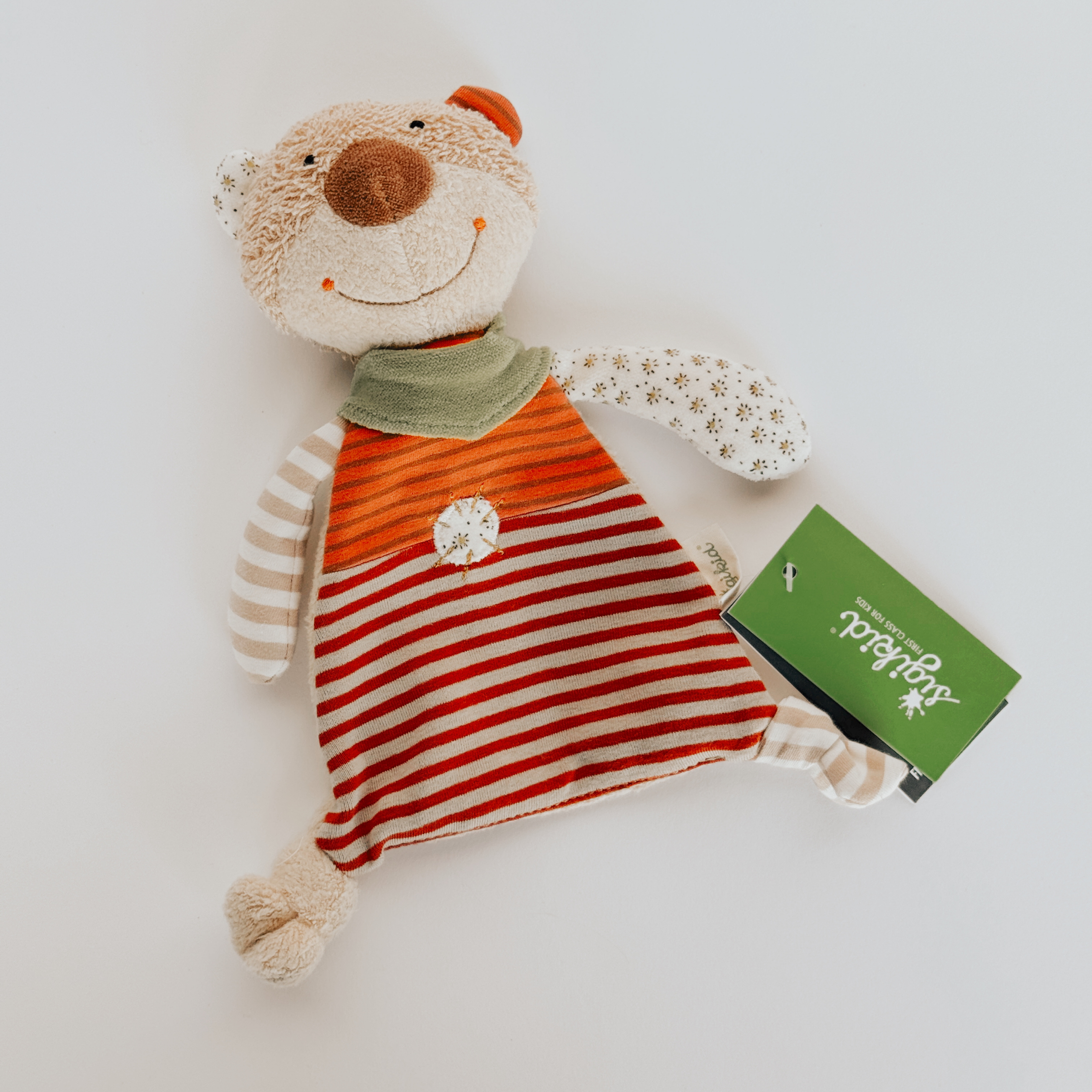 Organic Toy Blankie by Grace & Company, a plush bear with red-white stripes, green scarf, and tag on a white surface.