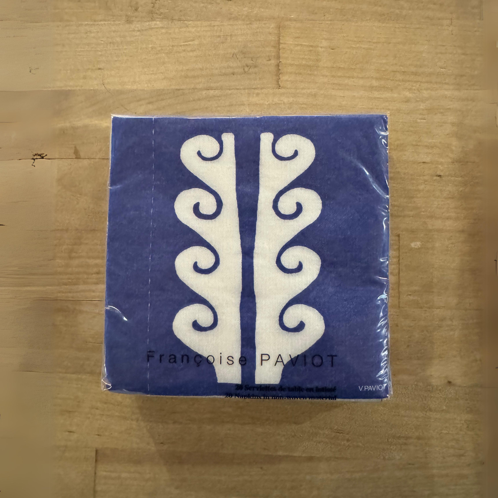 A Paviot - Paros Bleu napkin by Grace & Company with a white swirl pattern rests on a wooden surface.