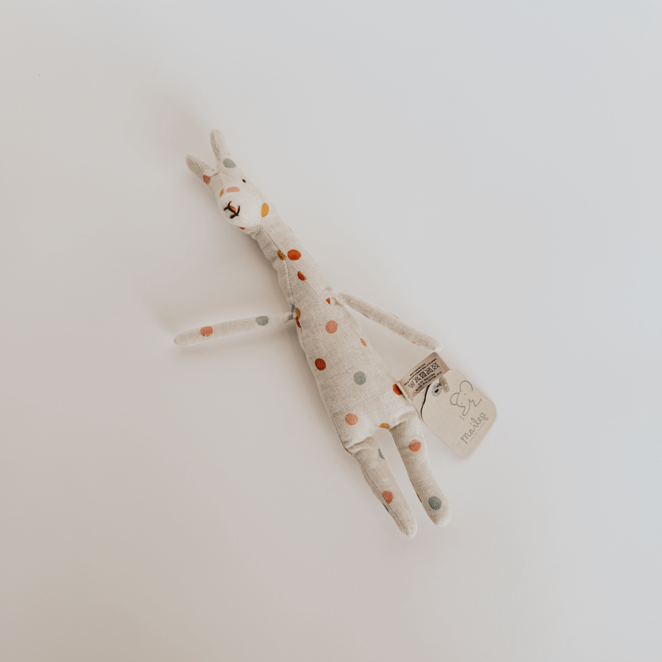 Maileg Safari Friends Mini Giraffe by Grace and Company Ltd with polka dots, tag attached, on a white surface.