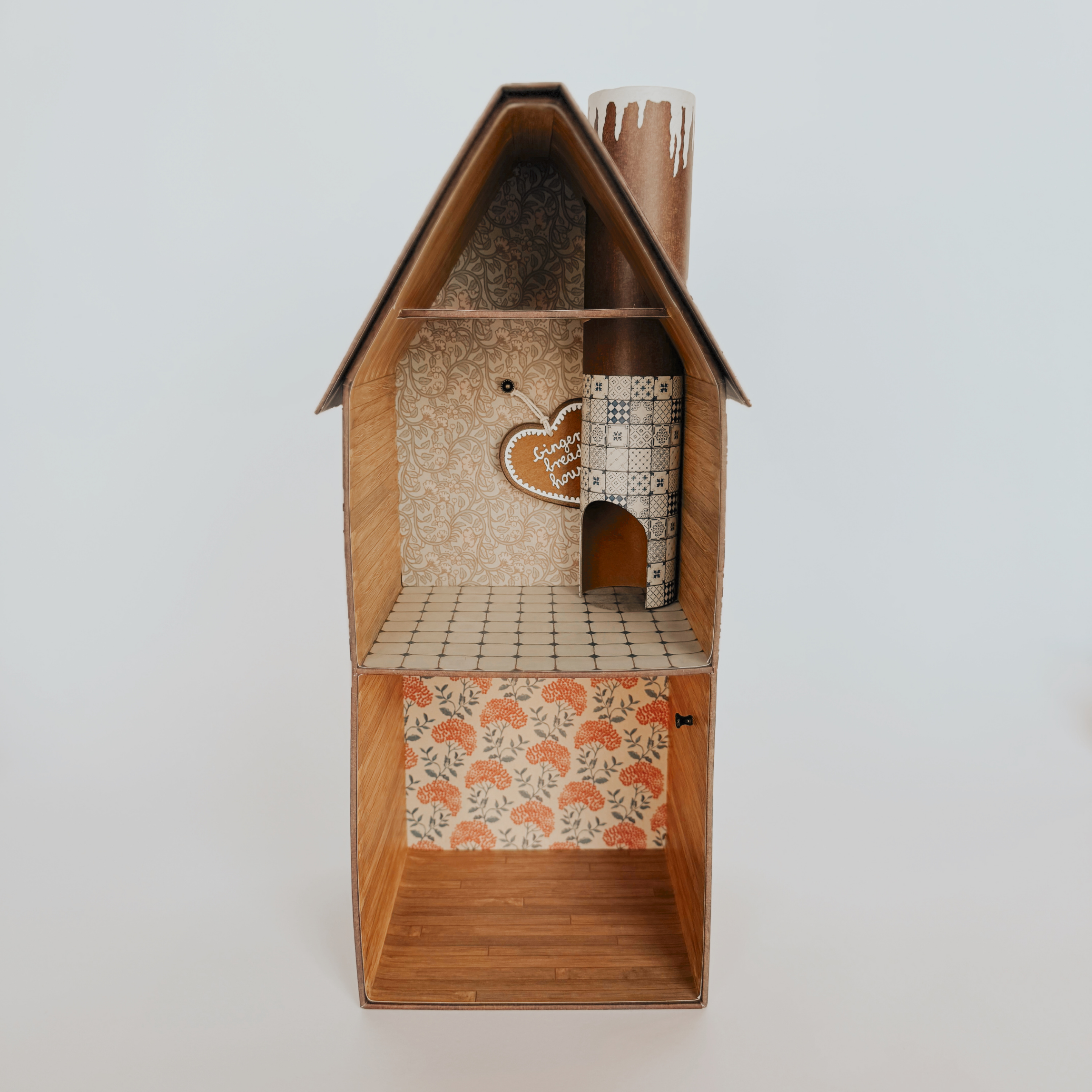 The Maileg Gingerbread House by Grace & Company is a two-story cardboard model with patterned walls and a faux chimney.