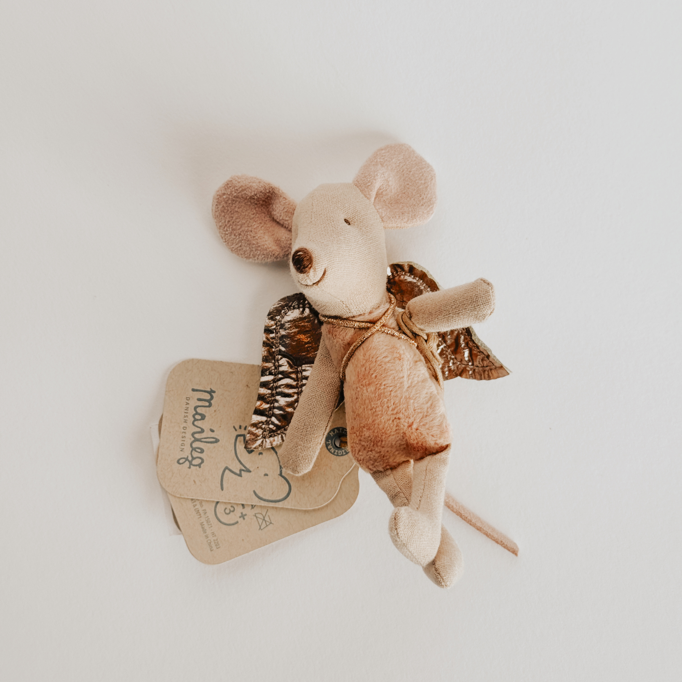 The Maileg - Fairy Mouse by Grace & Company, a small plush toy with wings, rests near tags on a white surface.