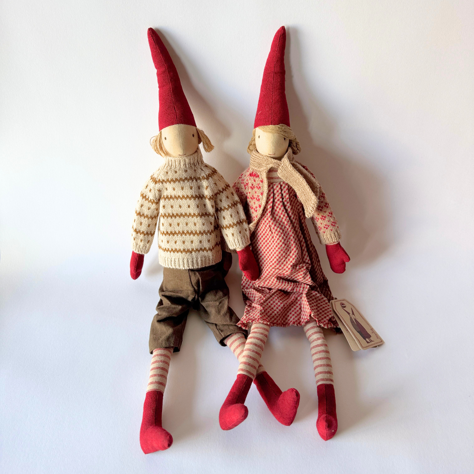 Maileg - Pixy Boy & Girl (Size 6) by Grace & Company sit side by side in winter clothes with red hats and stripe socks.