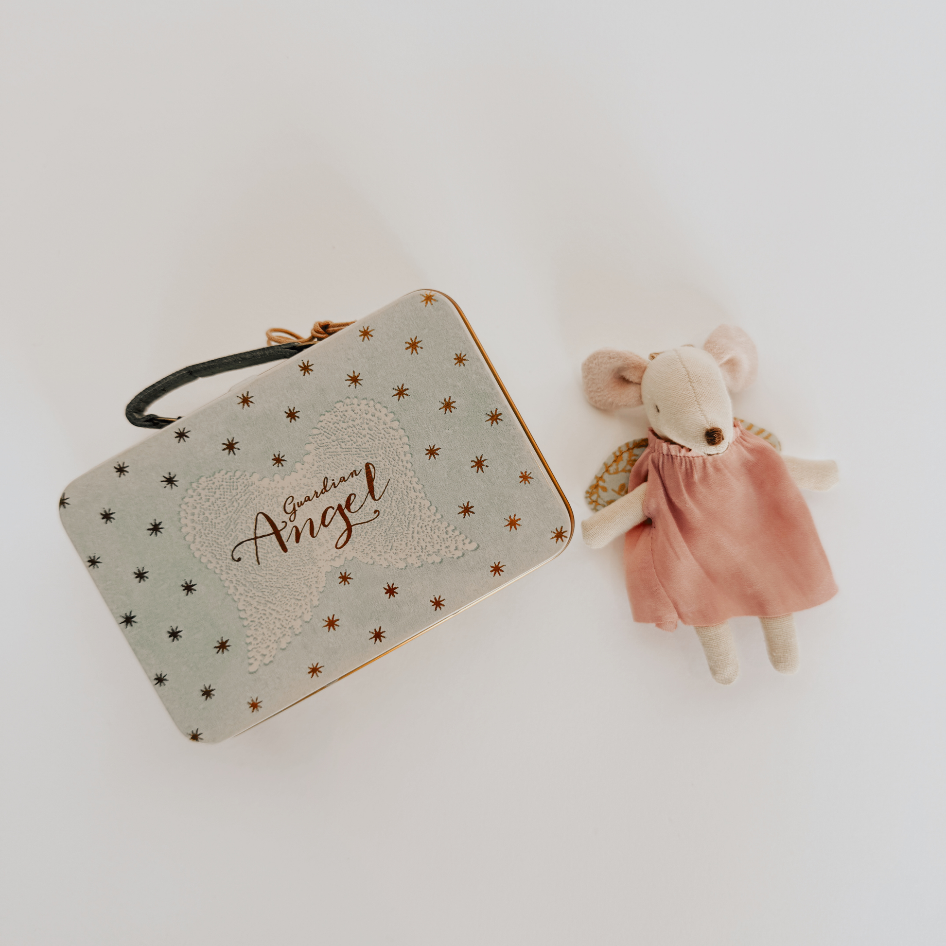 A Maileg - Guardian Mouse in a pink dress rests beside a star-patterned tin, by Grace & Company.