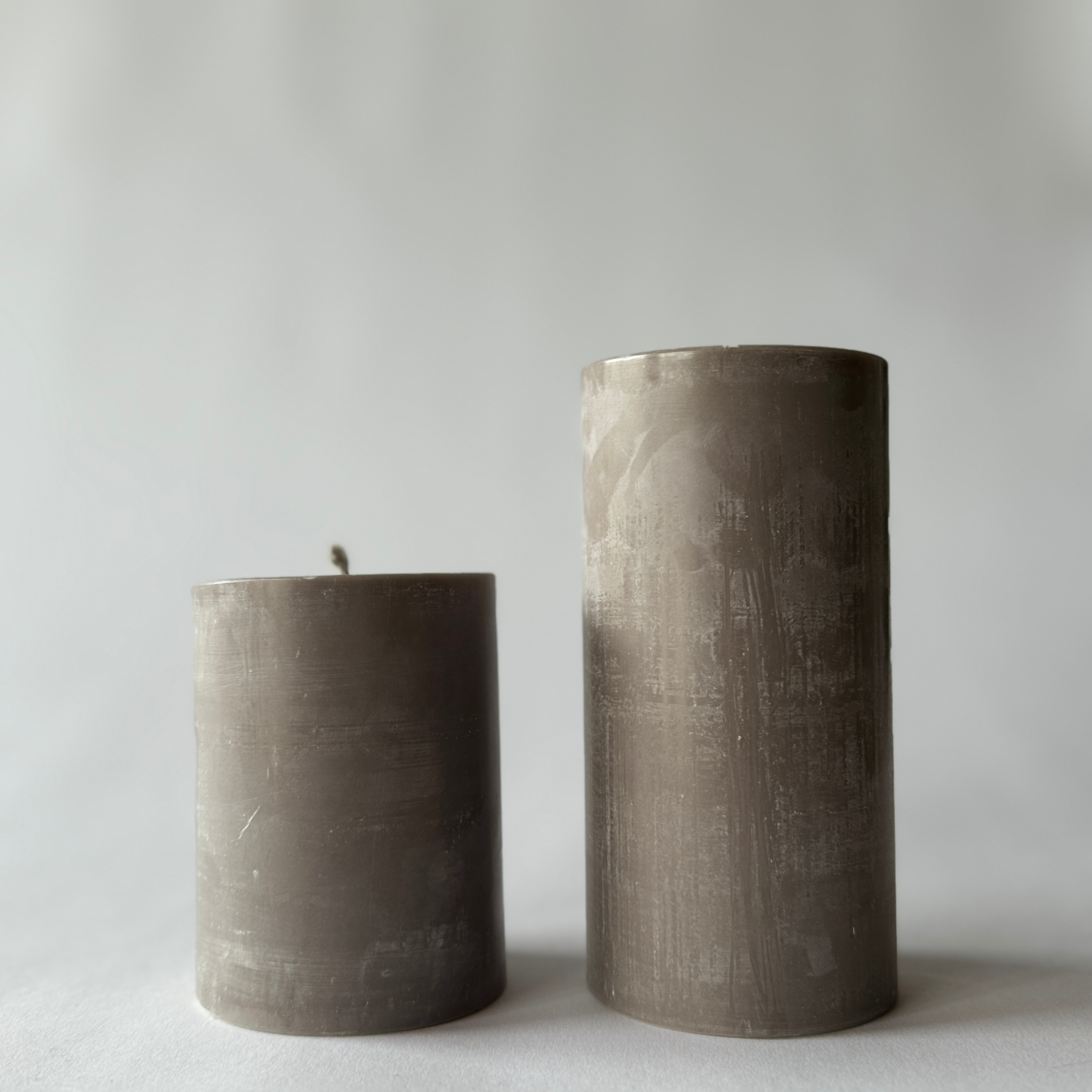 Two Grace & Company Standard Pillar Candles in gray, different heights, on a light surface with neutral background.