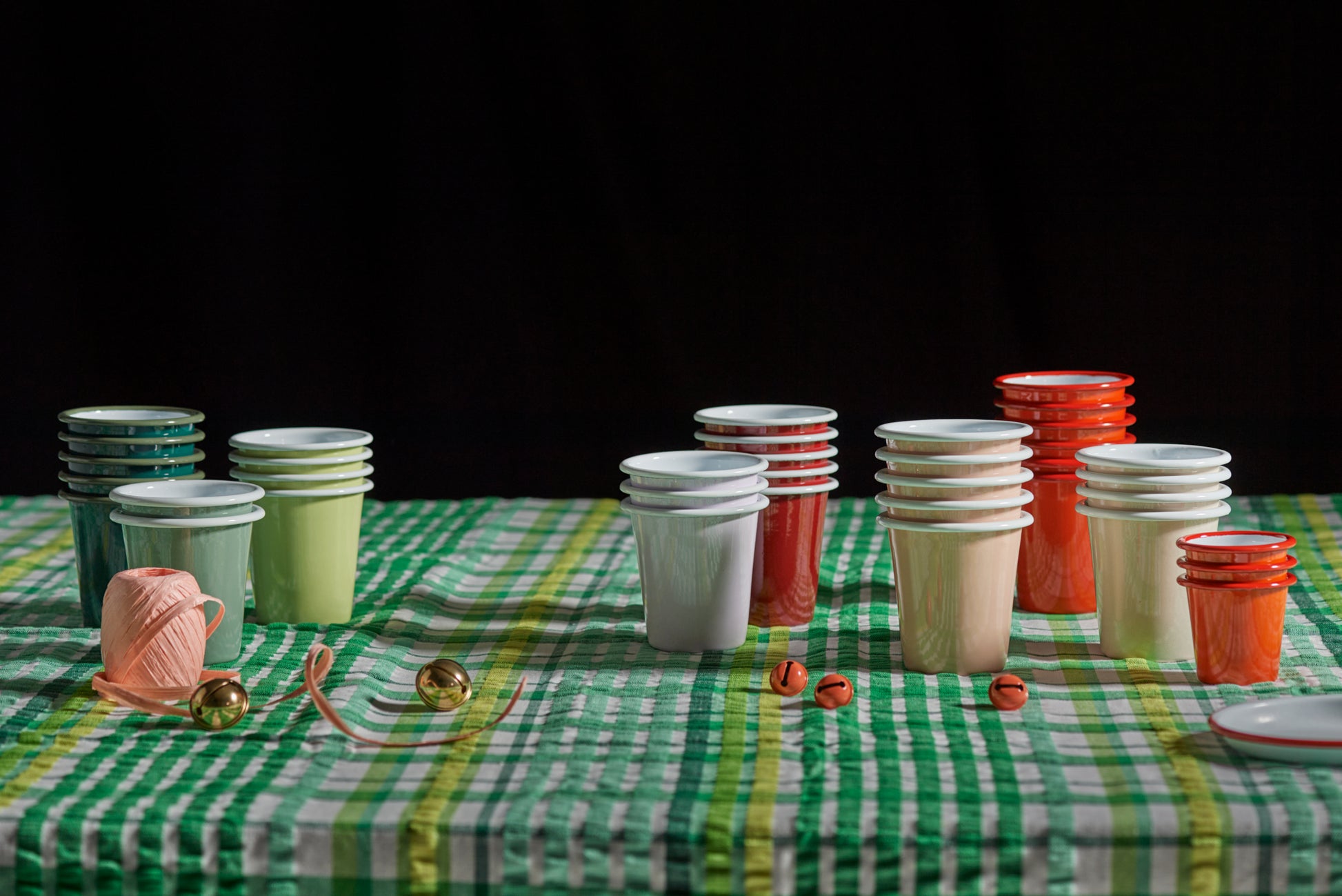 Grace & Company Falcon Enamelware Tumblers in vibrant colors on a green checked tablecloth with string and buttons.