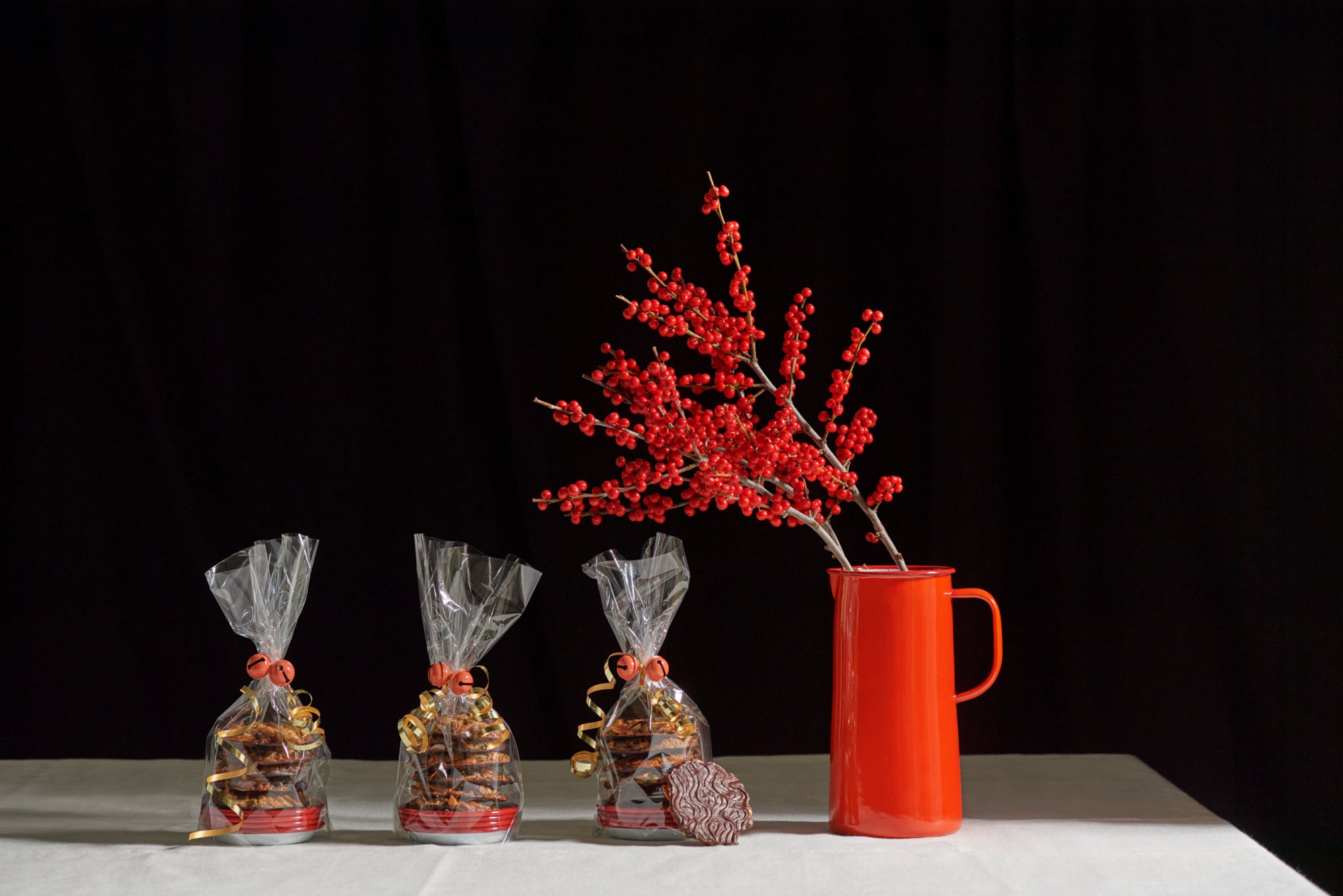 Three bags of cookies and a red pitcher with red berries on a white tablecloth against a black background.