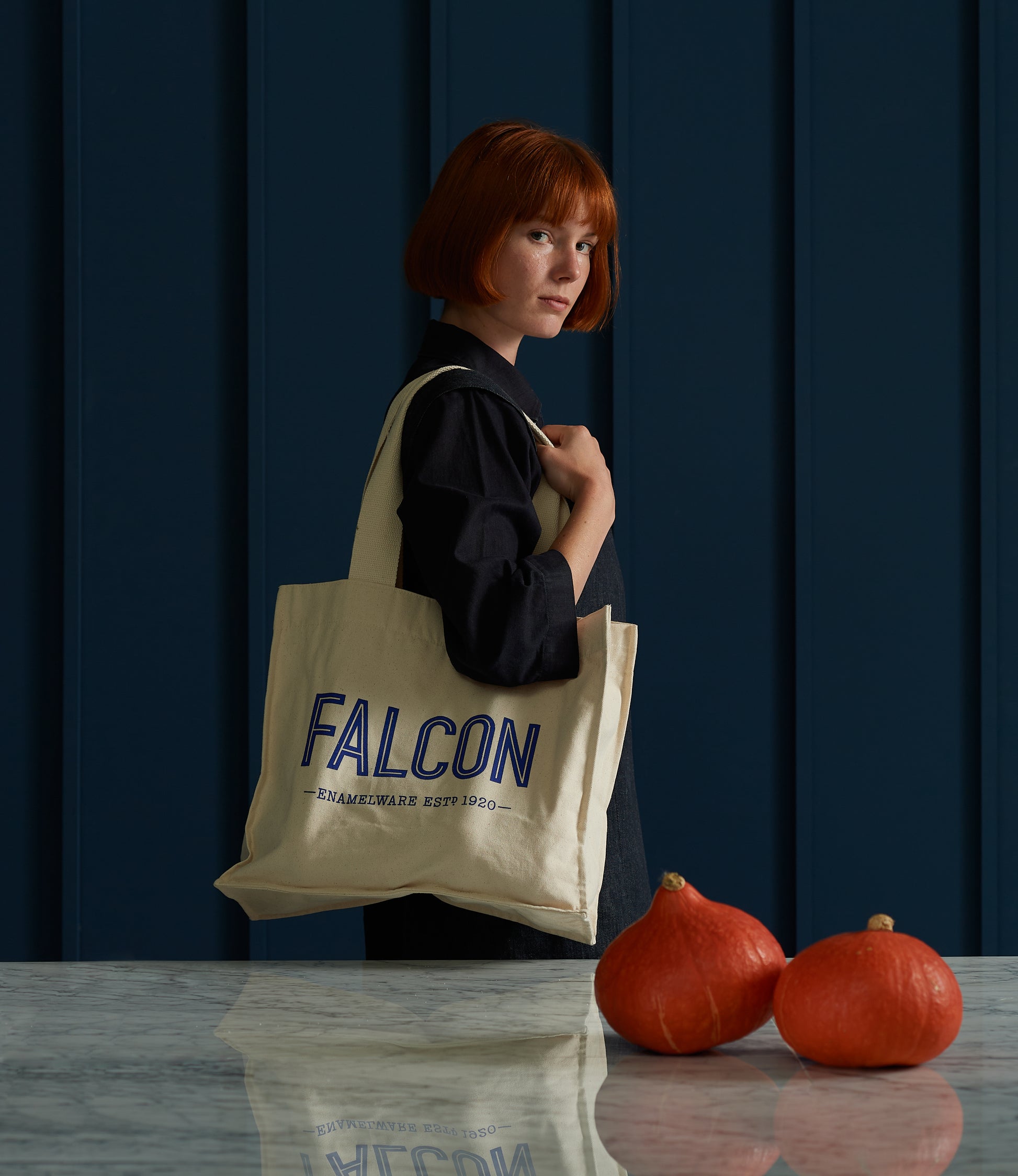 A red-haired woman holds a Falcon Enamelware Cotton Shopper by Grace & Company ltd beside a marble table with squash.