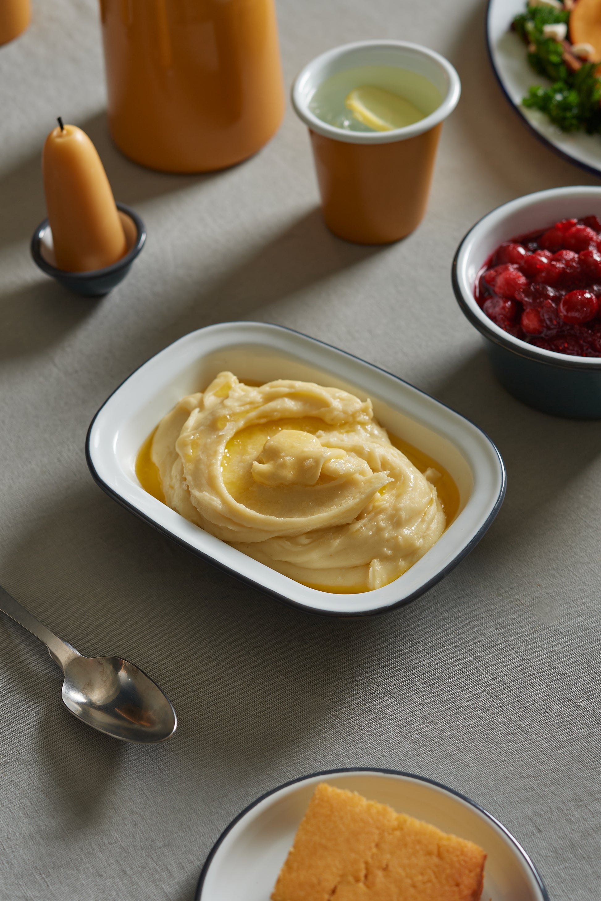 A Falcon Enamelware Pie Set by Grace & Company ltd holds mashed potatoes, cranberry sauce, cornbread, and a drink.