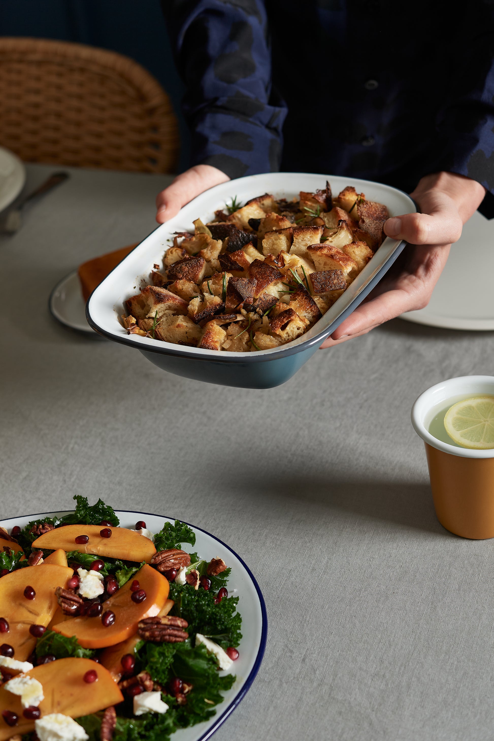 Someone serves a baked bread casserole in the Falcon Enamelware Pie Set by Grace & Company Ltd, with salad and lemon water.