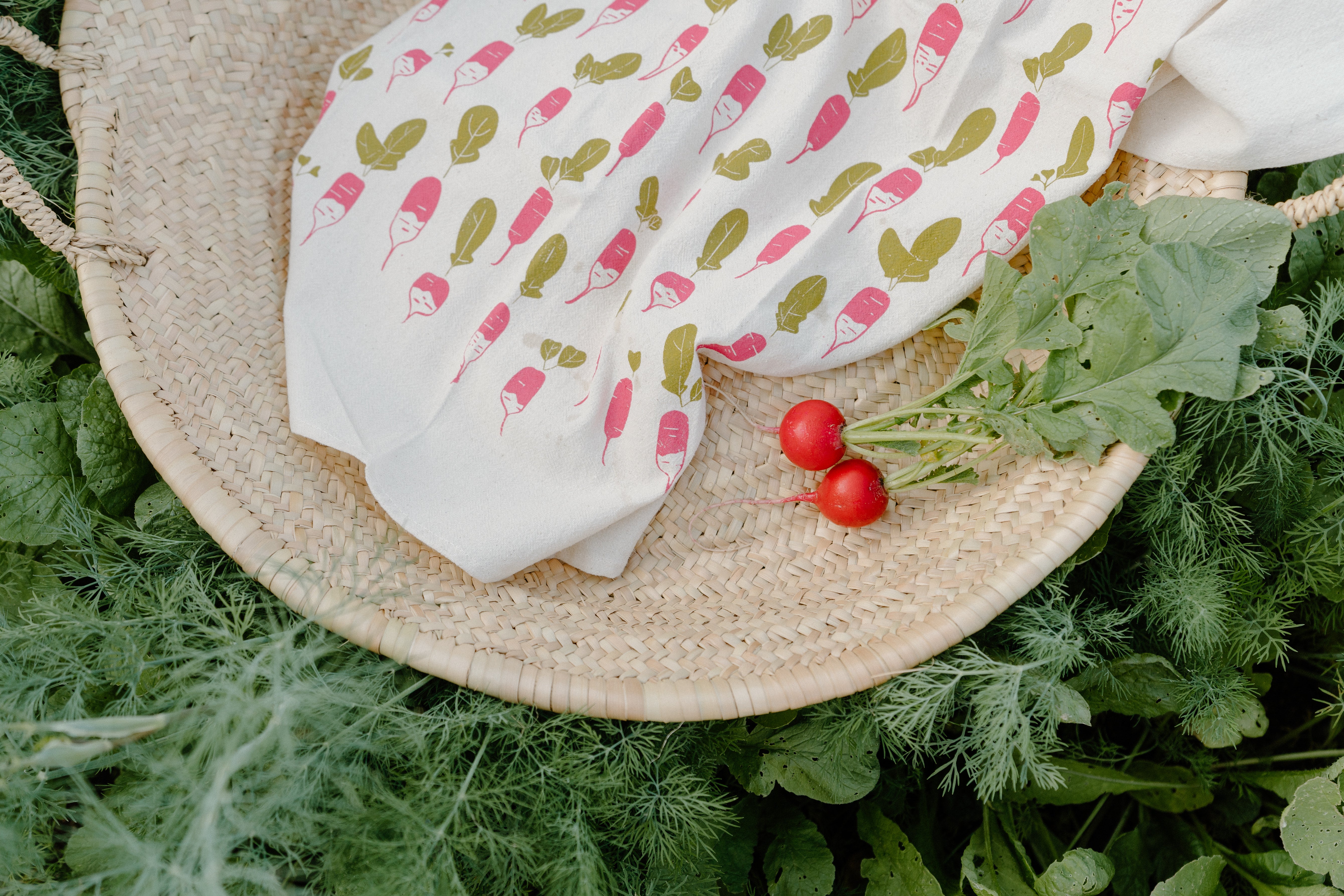 The Grace & Company Hand Painted Cotton Towel features radish designs beside fresh radishes in a woven basket.