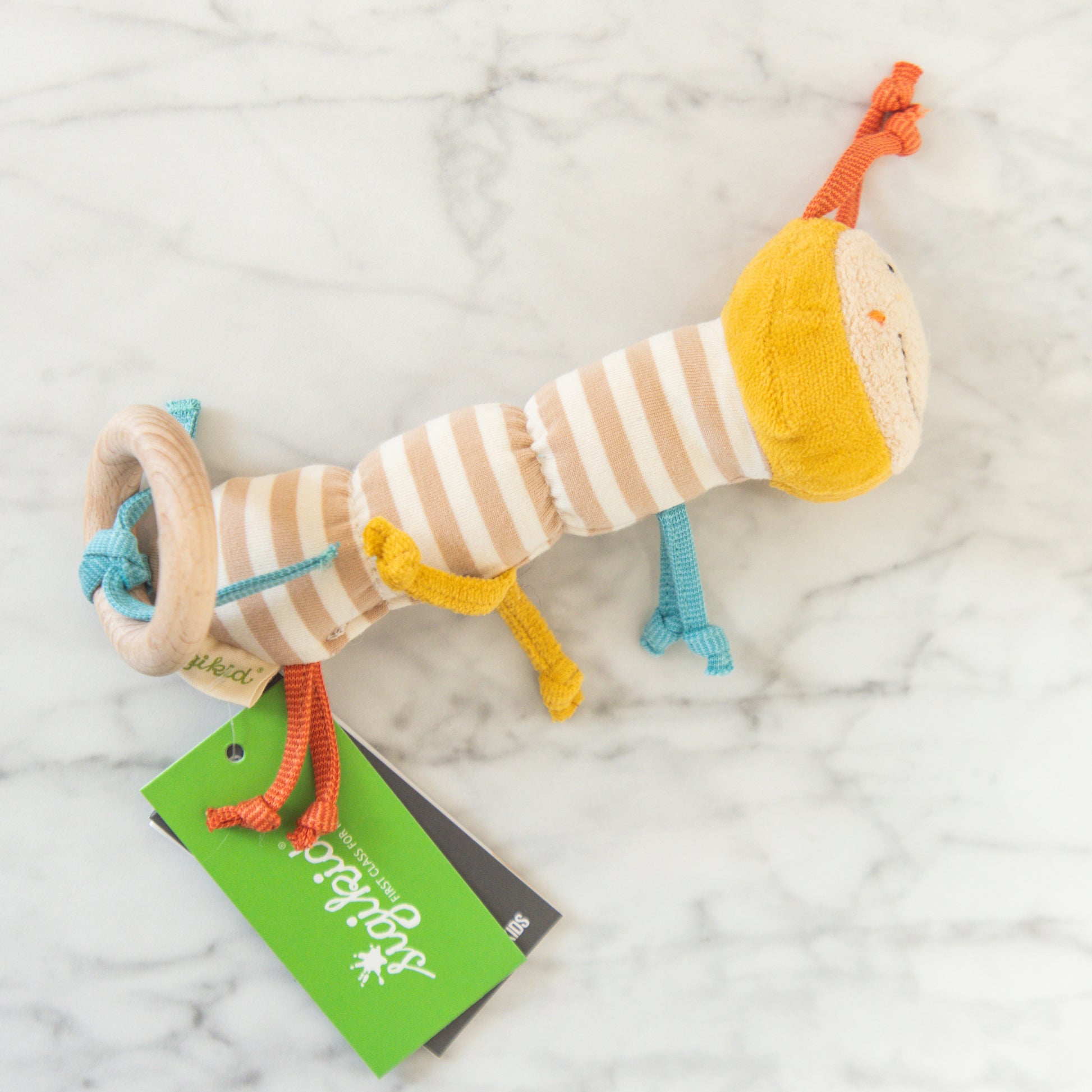 The Organic Caterpillar Rattle by Grace & Company features stripes, a yellow head, blue-orange limbs, and a green tag.
