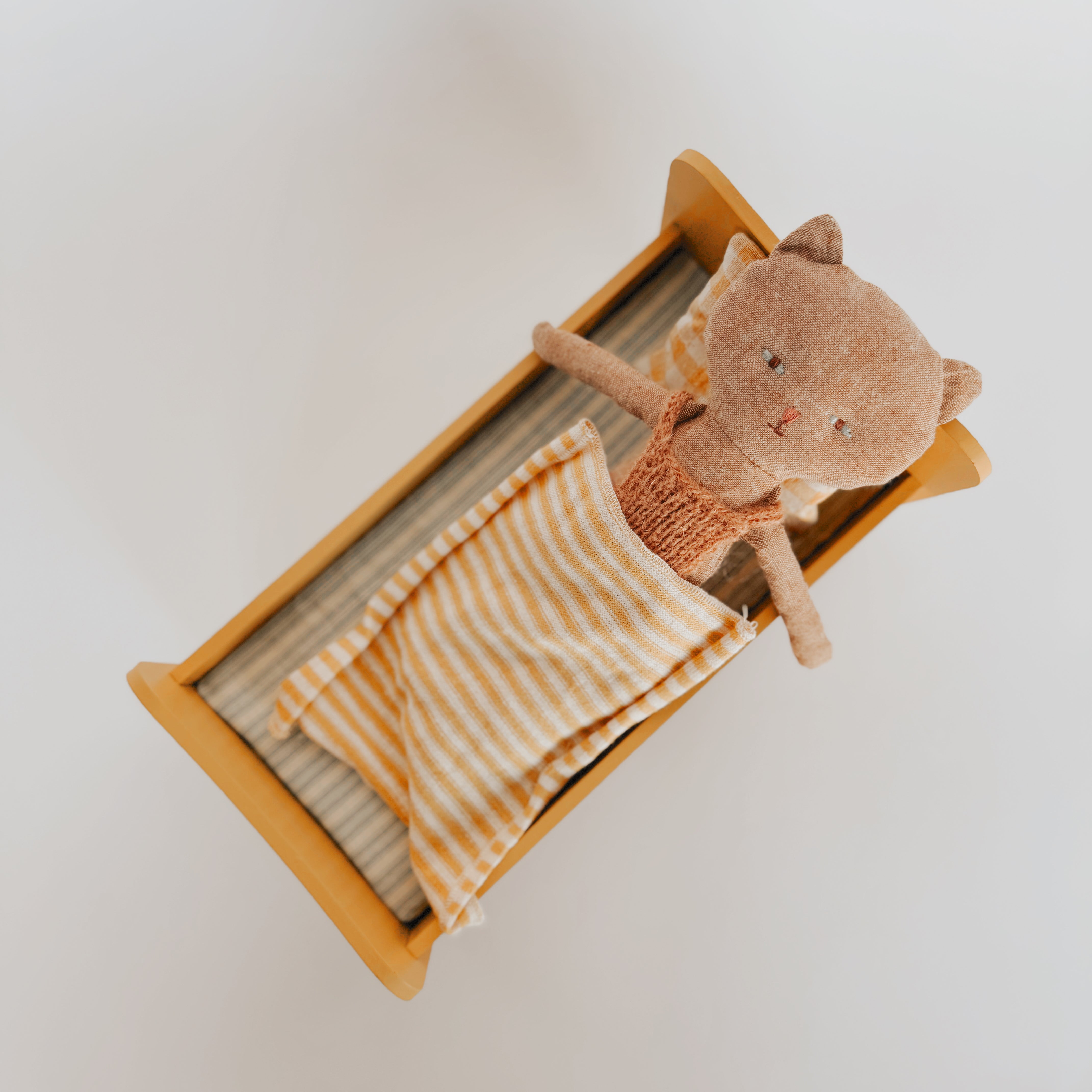 Maileg Wooden Bed Mini with Vintage Kitten in Sweater by Grace & Company Ltd, covered with a striped blanket.