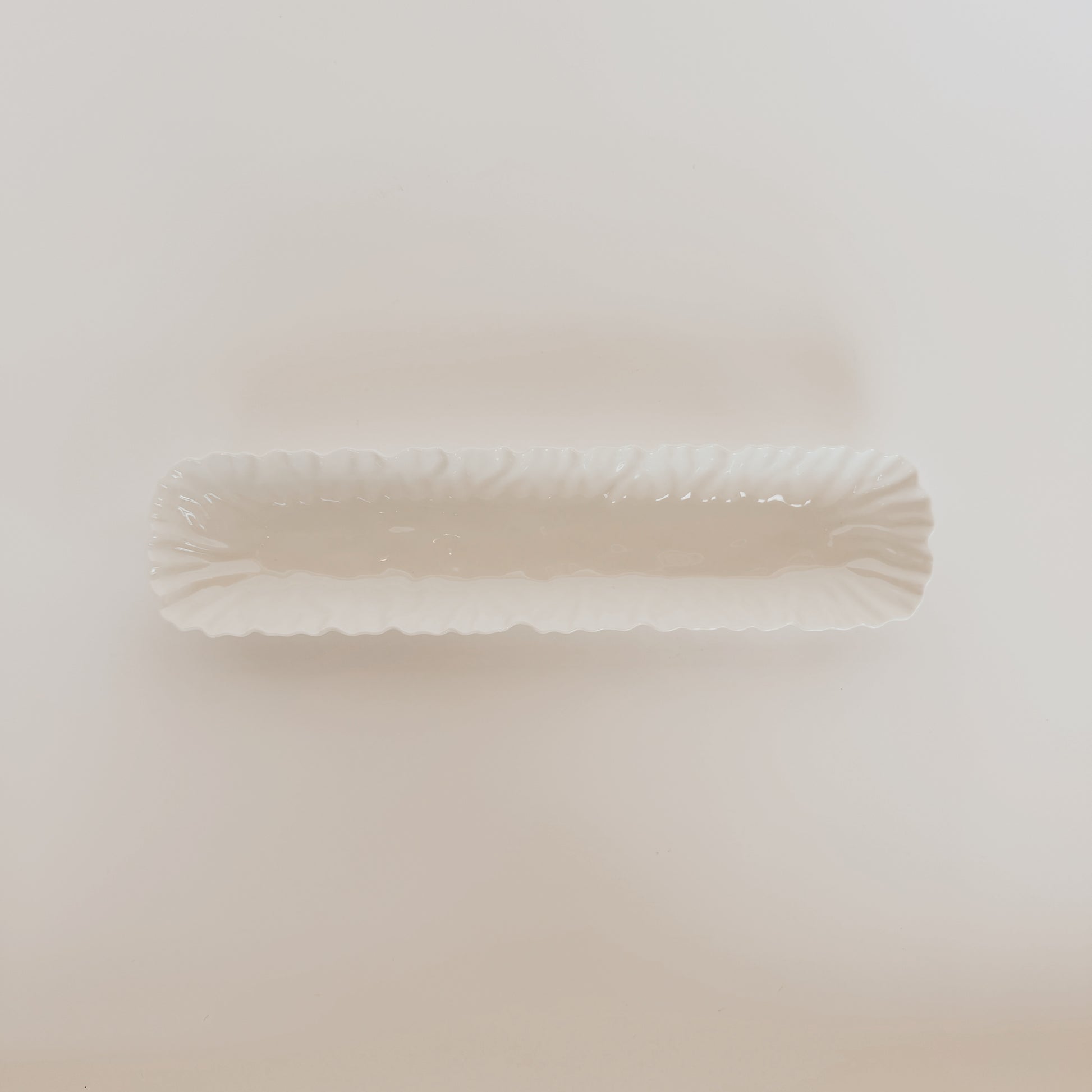 The Mascali Bianca Serve Collection by Grace and Company Ltd features a long, scalloped white ceramic dish.