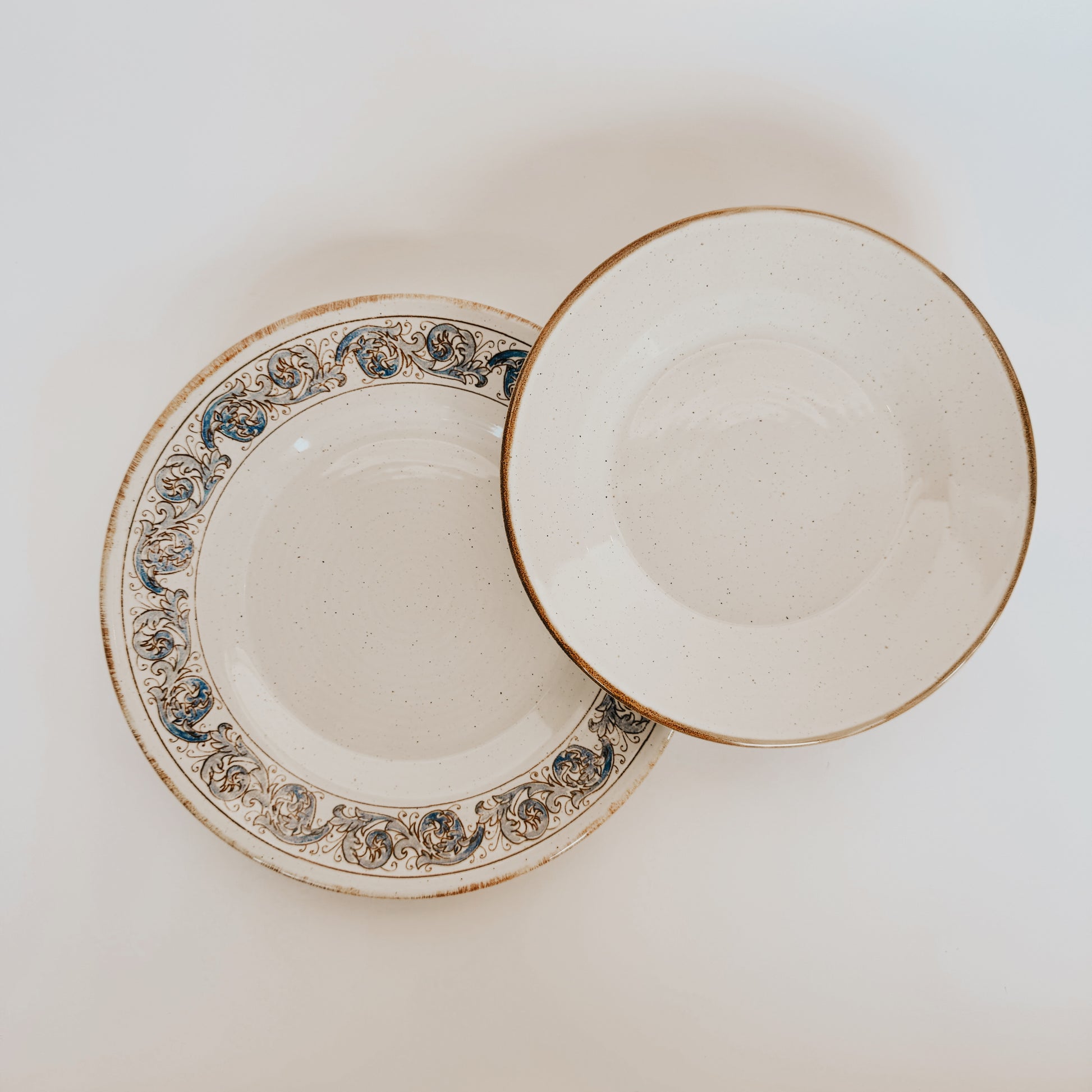 Two Sardegna Dinner Set plates by Grace & Company, one floral, one plain, overlap on a white background.