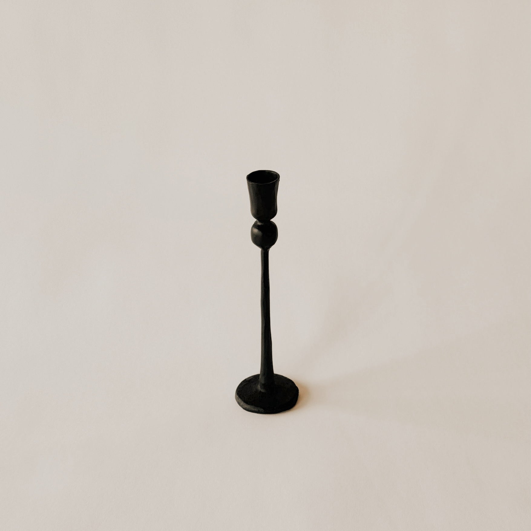 A Canmore Taper Candle Holder by Grace & Company in black metal on a plain, light beige background.