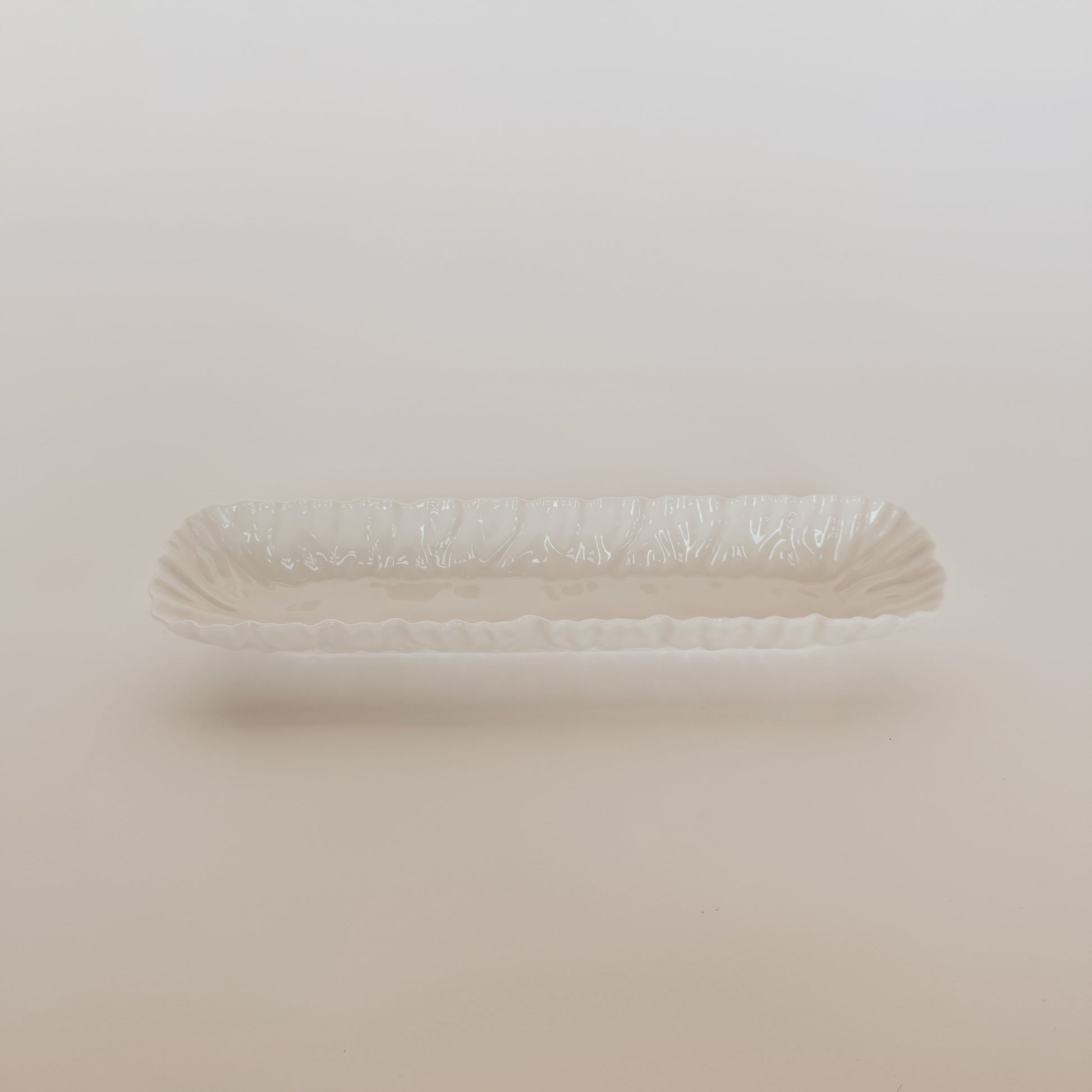 The Mascali Bianca Serve Collection by Grace and Company Ltd features a white ceramic serving dish with ruffled edges.