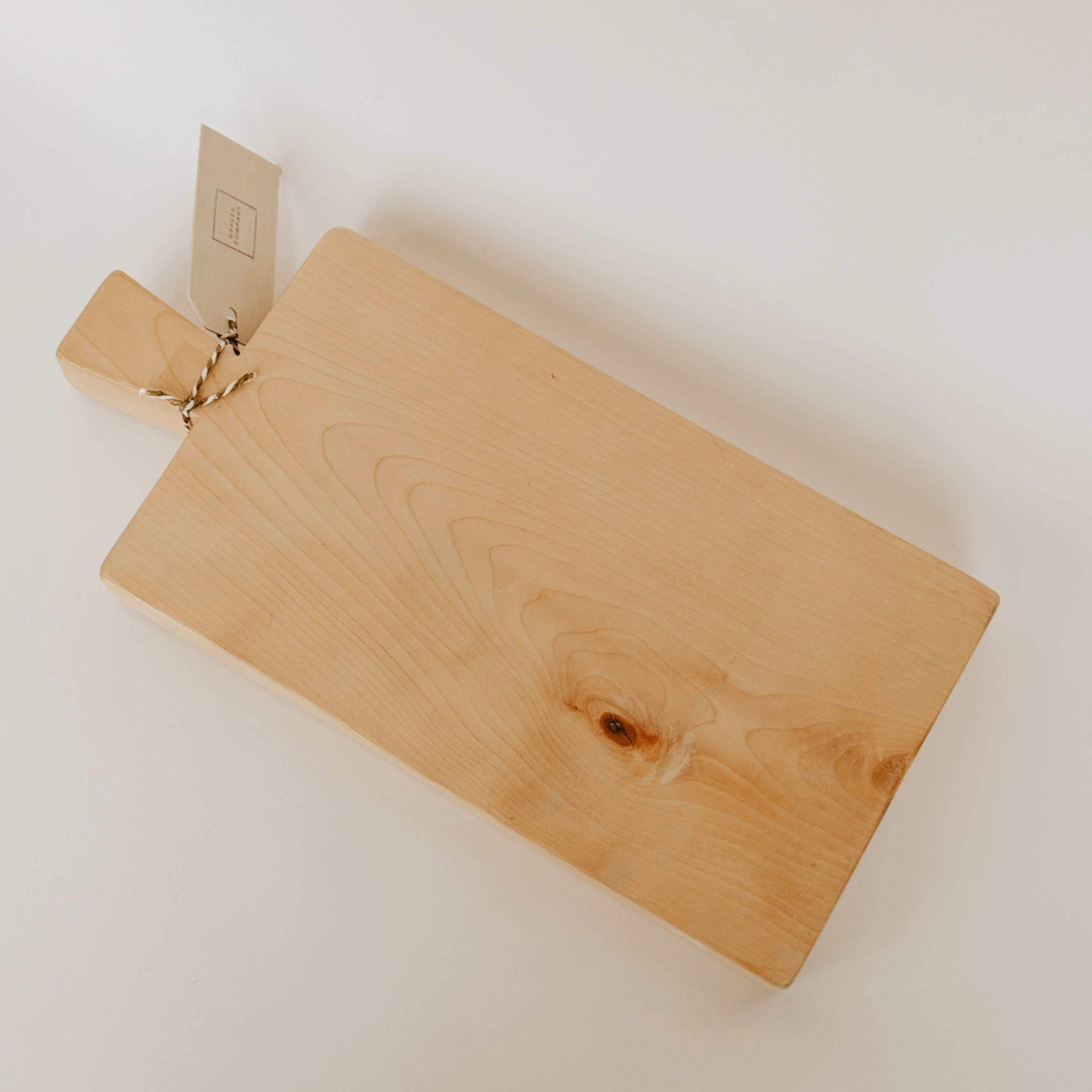 A Custom Birch Board by Grace & Company, featuring a handle and tag, sits on a light surface.
