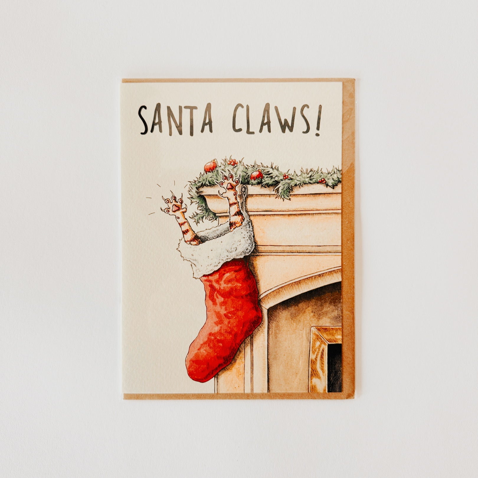 A holiday card with Santa Claws! showing a cats paws sticking out of a red stocking hanging on a mantel.