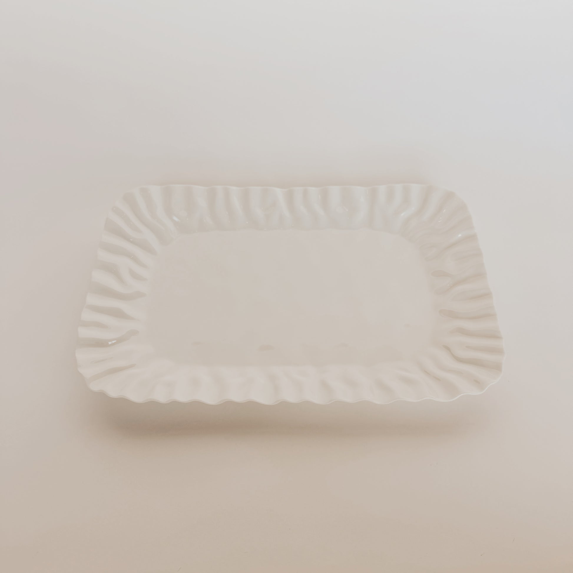 The Mascali Bianca Serve plate by Grace and Company Ltd features wavy, textured edges and a white ceramic square design.