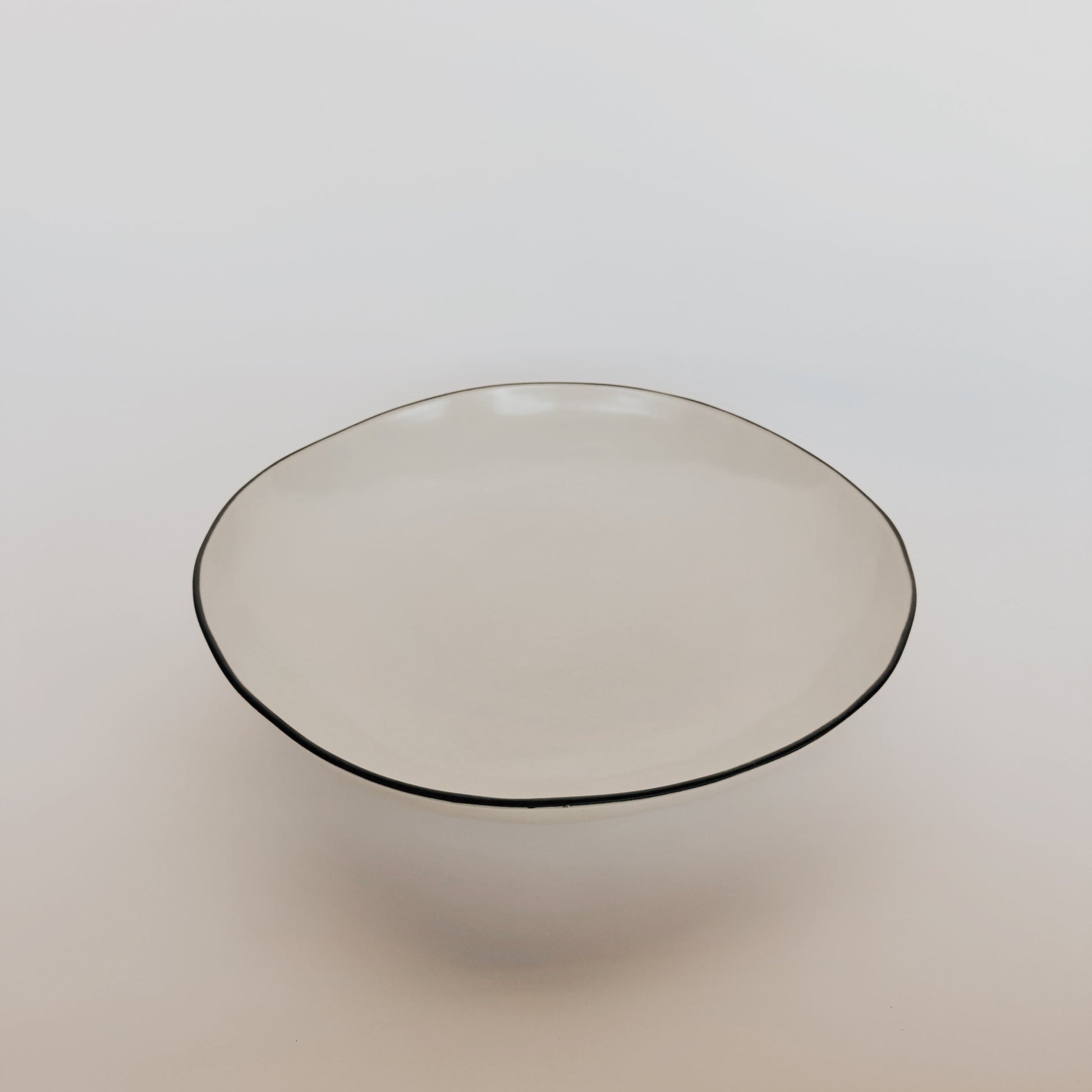 The Stacked Organic Serving Bowl - Salt by Grace & Company ltd is a round, shallow white ceramic bowl with uneven edges.