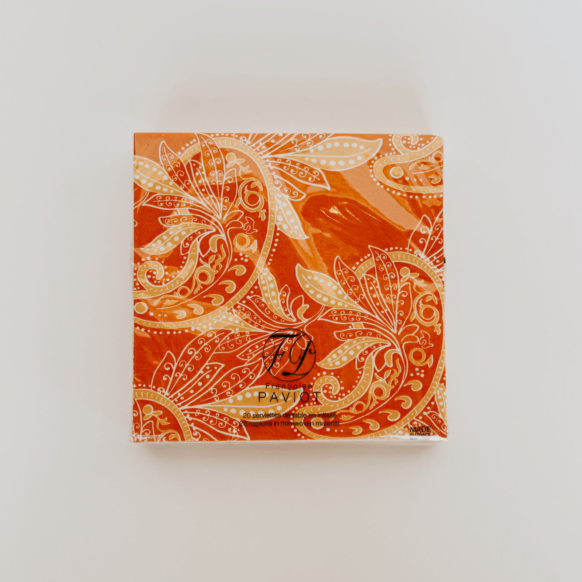 Grace & Company Paviot - Indi Napkins: square box with orange, gold paisley on white, small black logo at bottom.