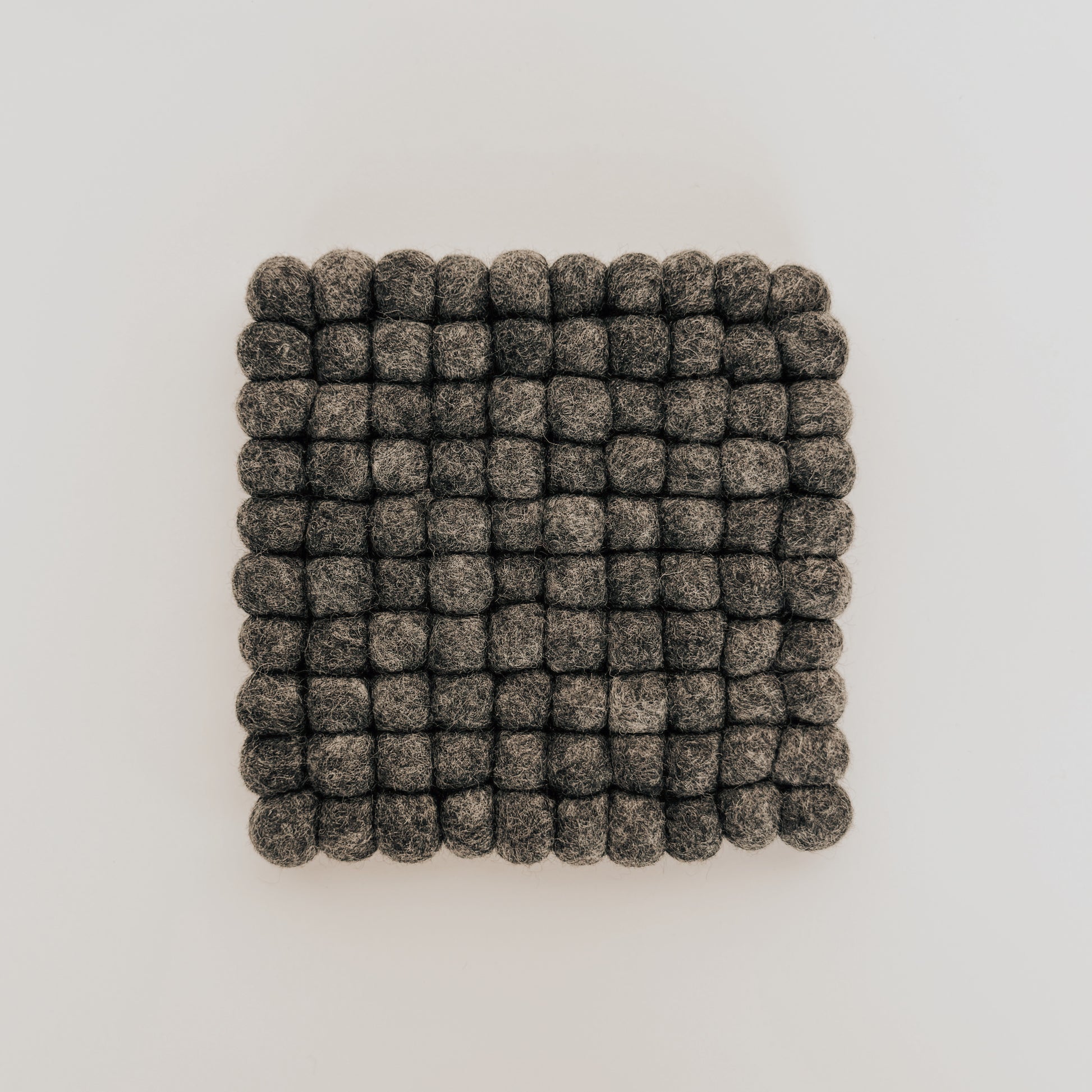 The Grace & Company Wool Felt Ball Trivet features gray, round felt balls arranged in a square on a white background.