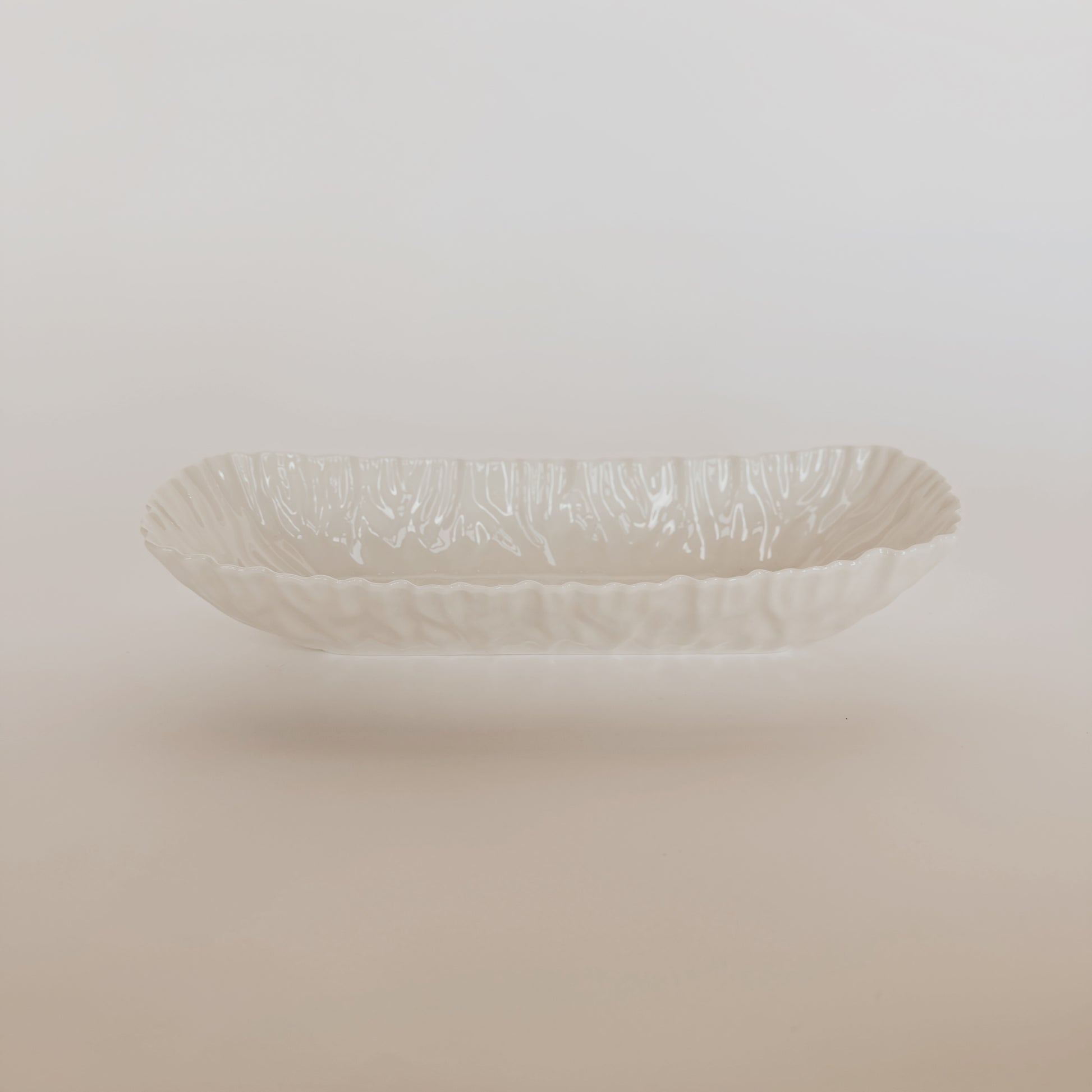 The Mascali Bianca Serve Collection by Grace and Company Ltd features a white, oval ceramic dish with wavy edges.