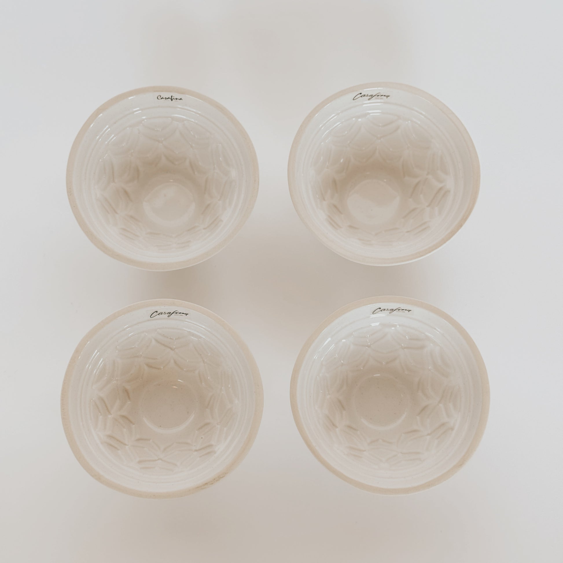 The Grace & Company Casafina Fatoria Cake Pan Set: four white pans with geometric patterns, arranged in a square.