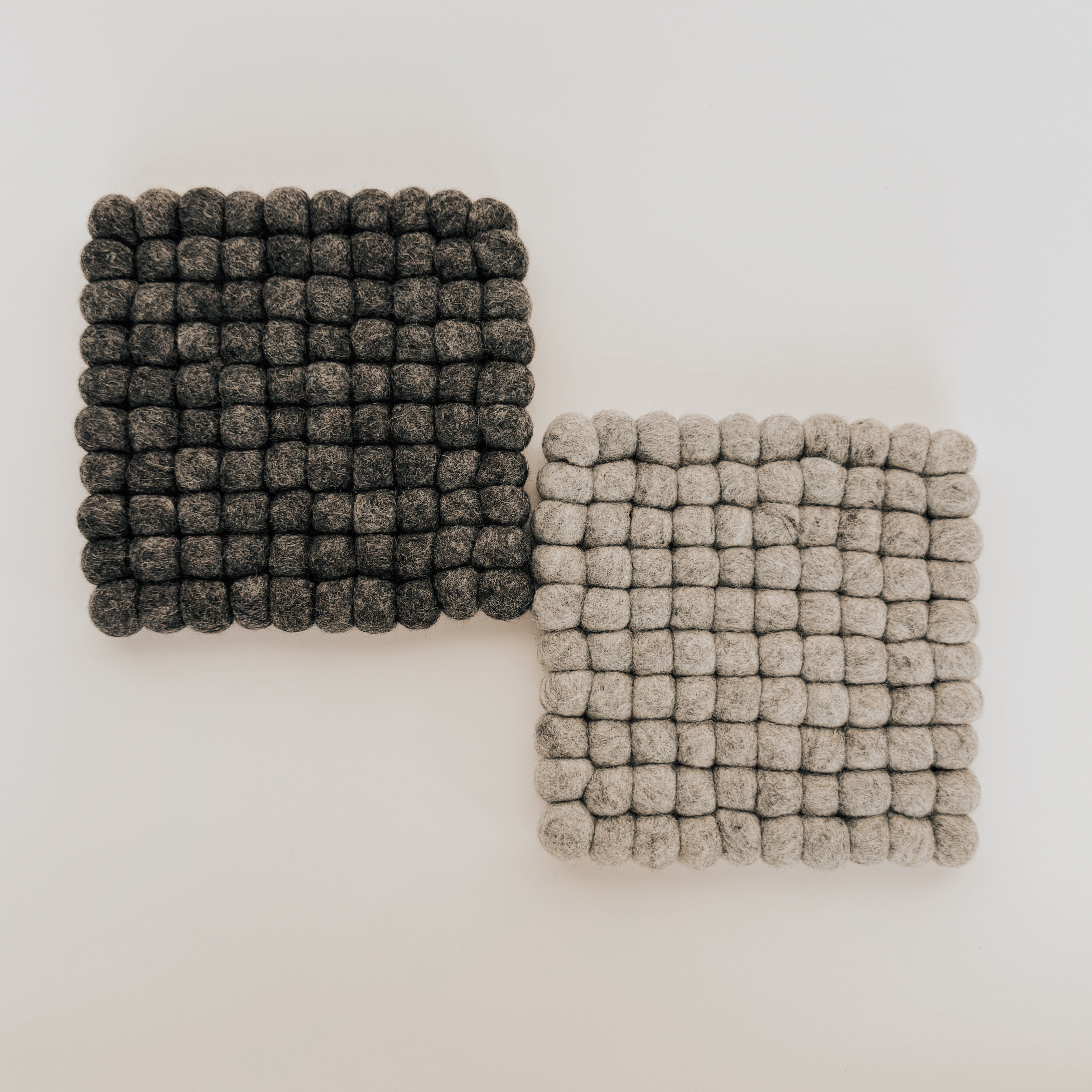 Two Grace & Company Wool Felt Ball Trivets, one dark gray and one light gray, are side by side on a white background.