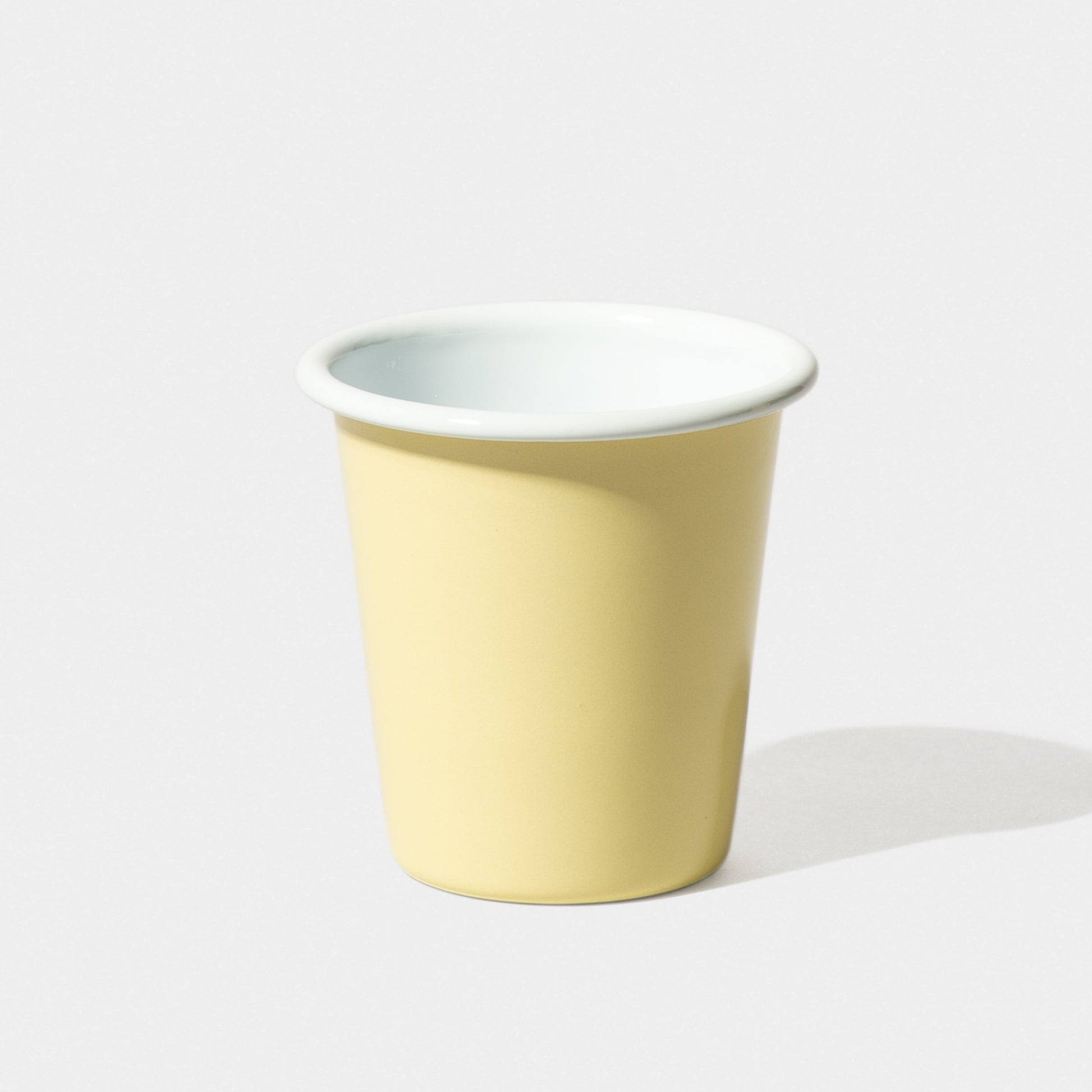 A yellow Falcon Enamelware Tumbler by Grace & Company with a white interior sits on a light surface, casting a soft shadow.