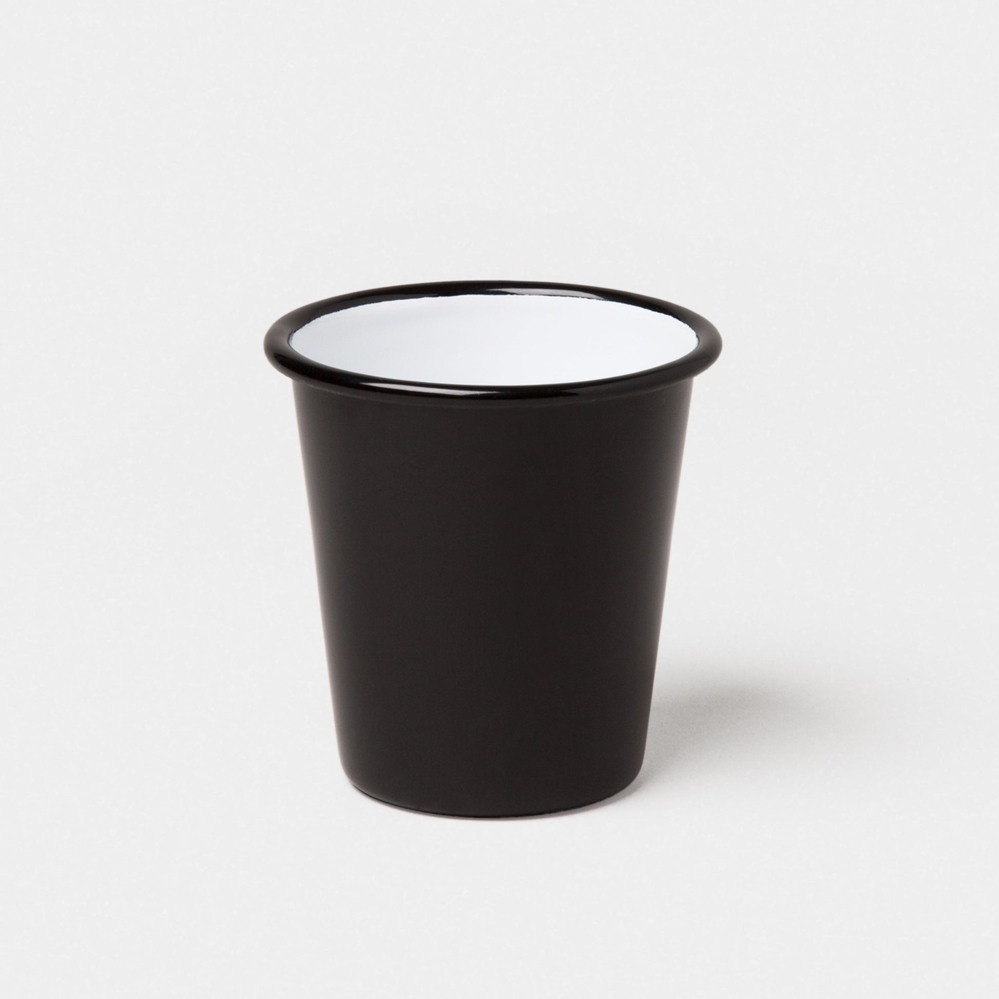 A Falcon Enamelware Tumbler by Grace & Company, black outside with white inside, set on a plain white background.