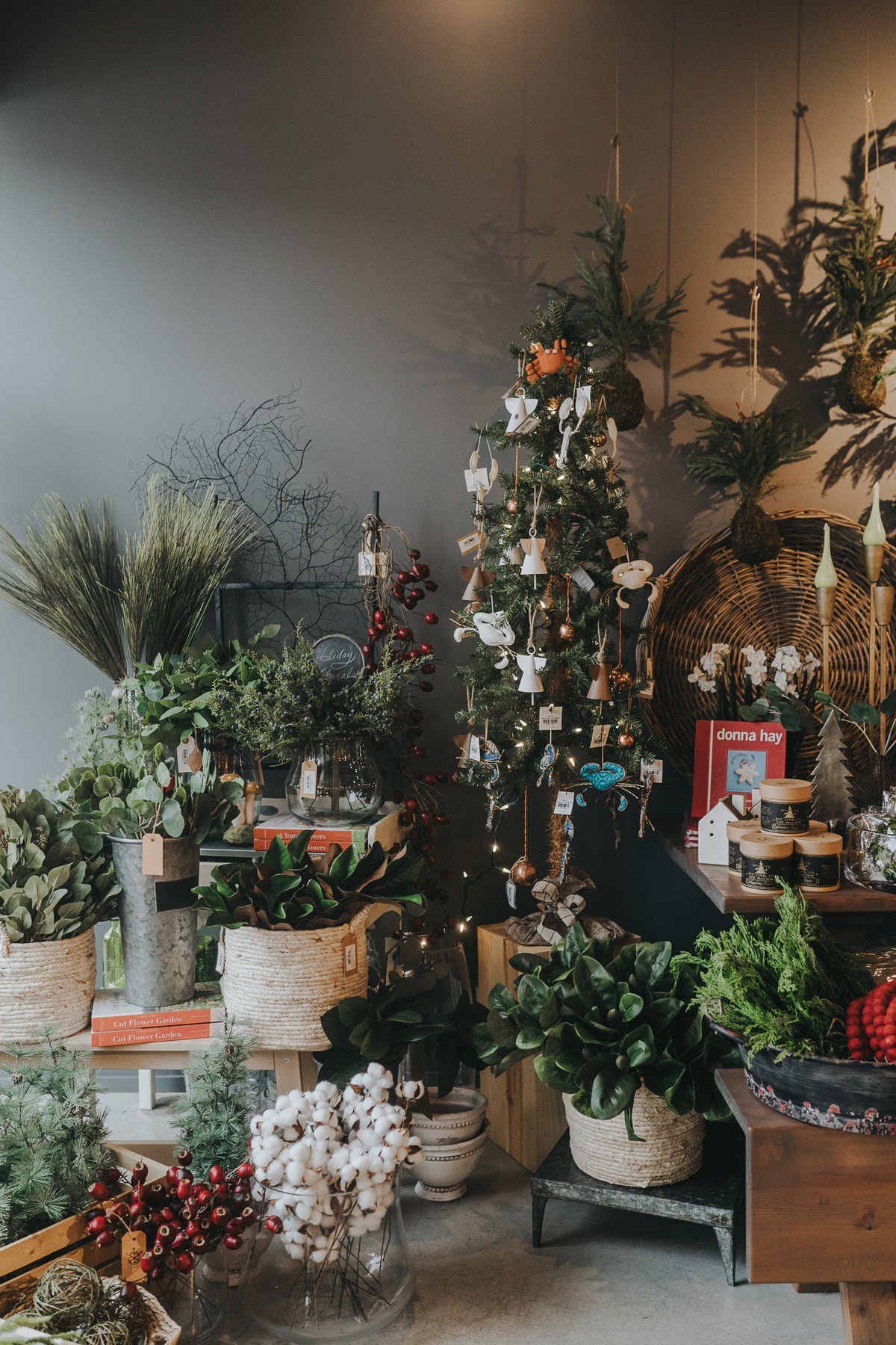 Indoor plant shop with potted greenery, small decorated Christmas tree, and various festive holiday decorations.