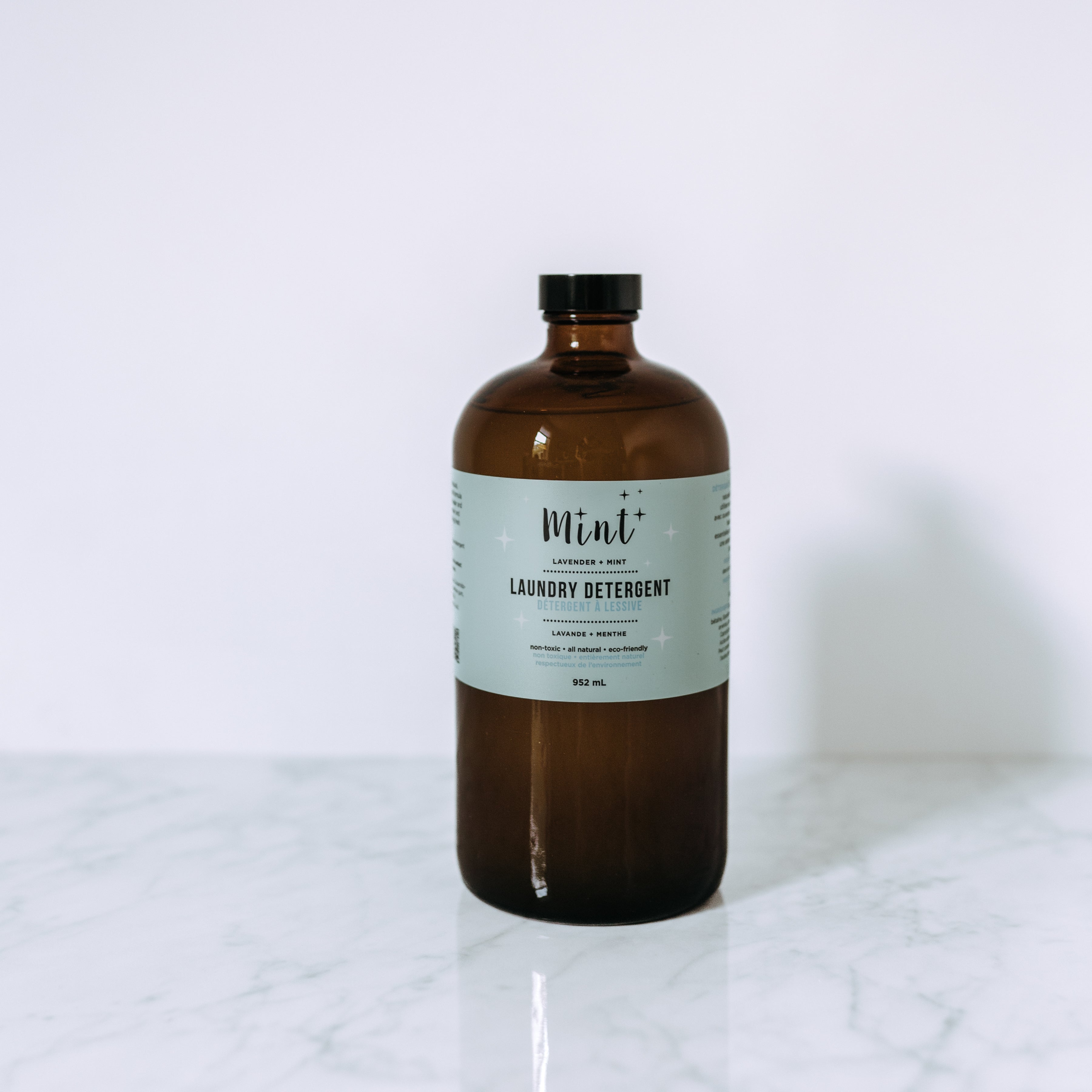 A brown glass bottle of Grace & Company Mint - Cleaning Products sits on a white marble surface.