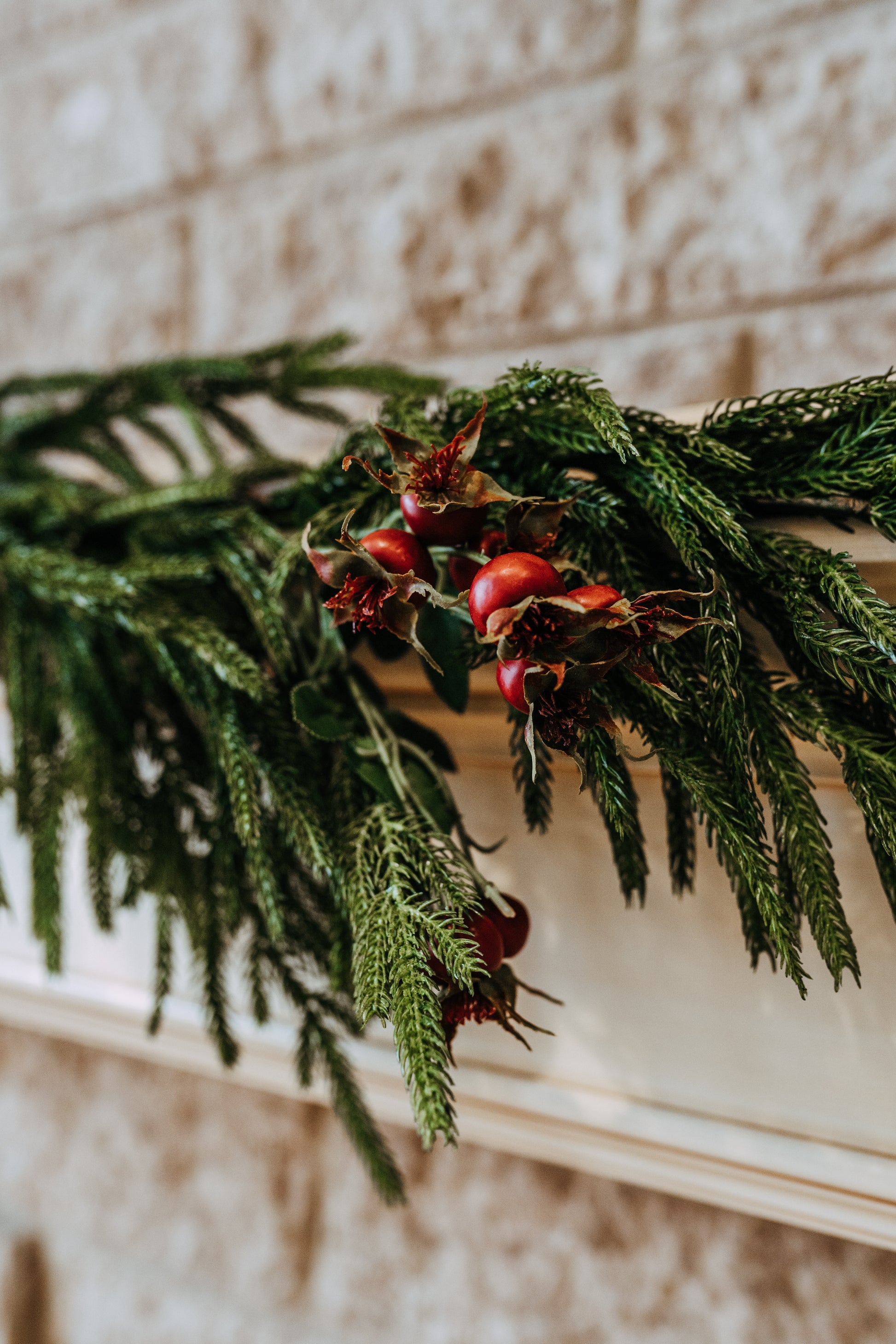 A close-up of Grace & Company’s Fresh Touch Norfolk Pine Collection garland with red berries on a beige mantel.