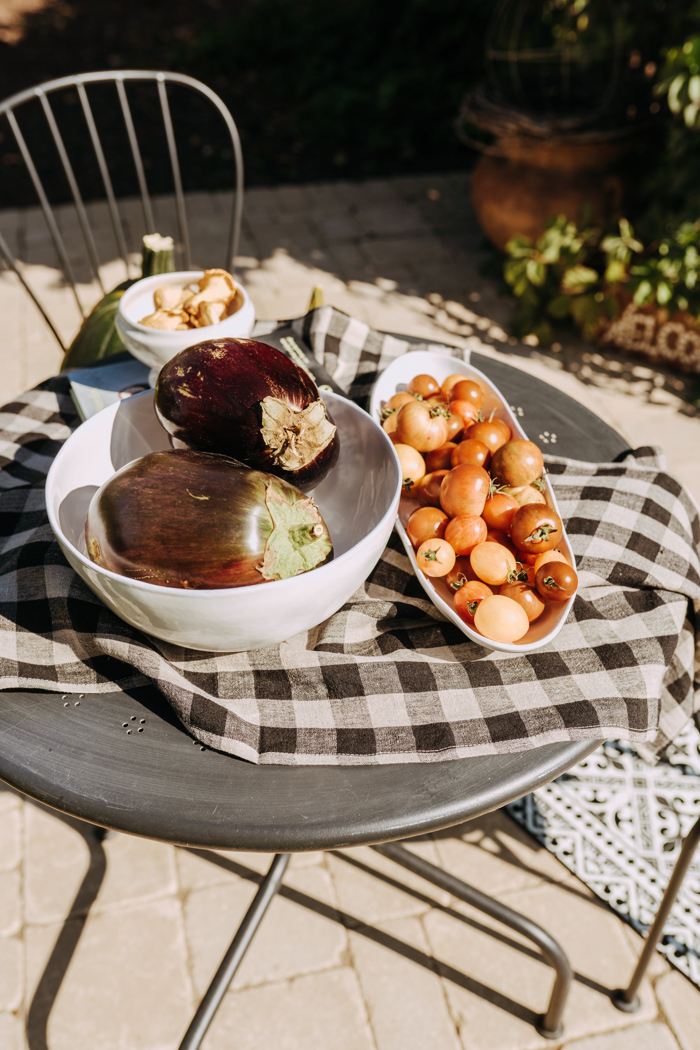 Grace & Company Linen Way - Table Linen Checkered displayed outdoors with bowls of eggplants, cherry tomatoes, and nuts.