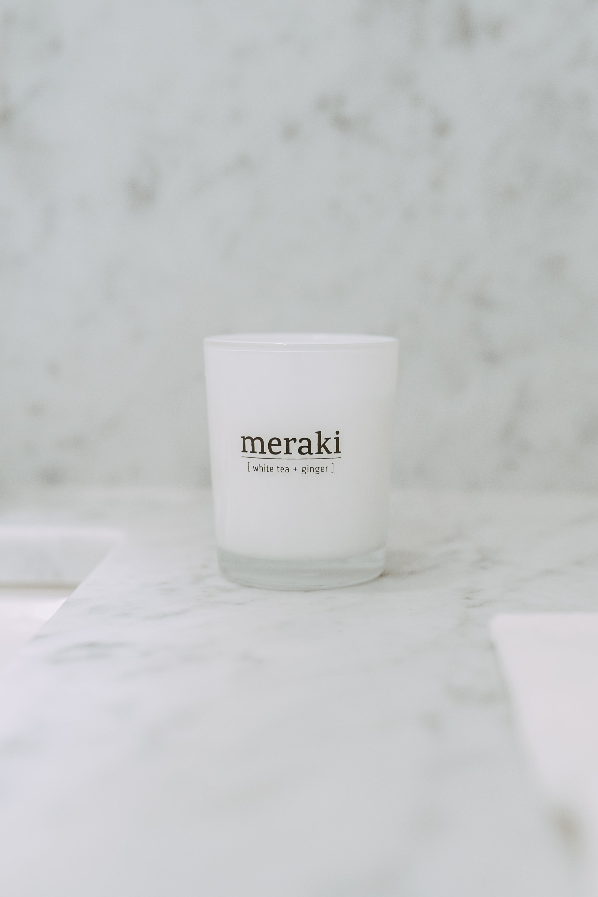 A Grace and Company Ltd Meraki - fragrance candle white tea + ginger sits on a white marble surface.