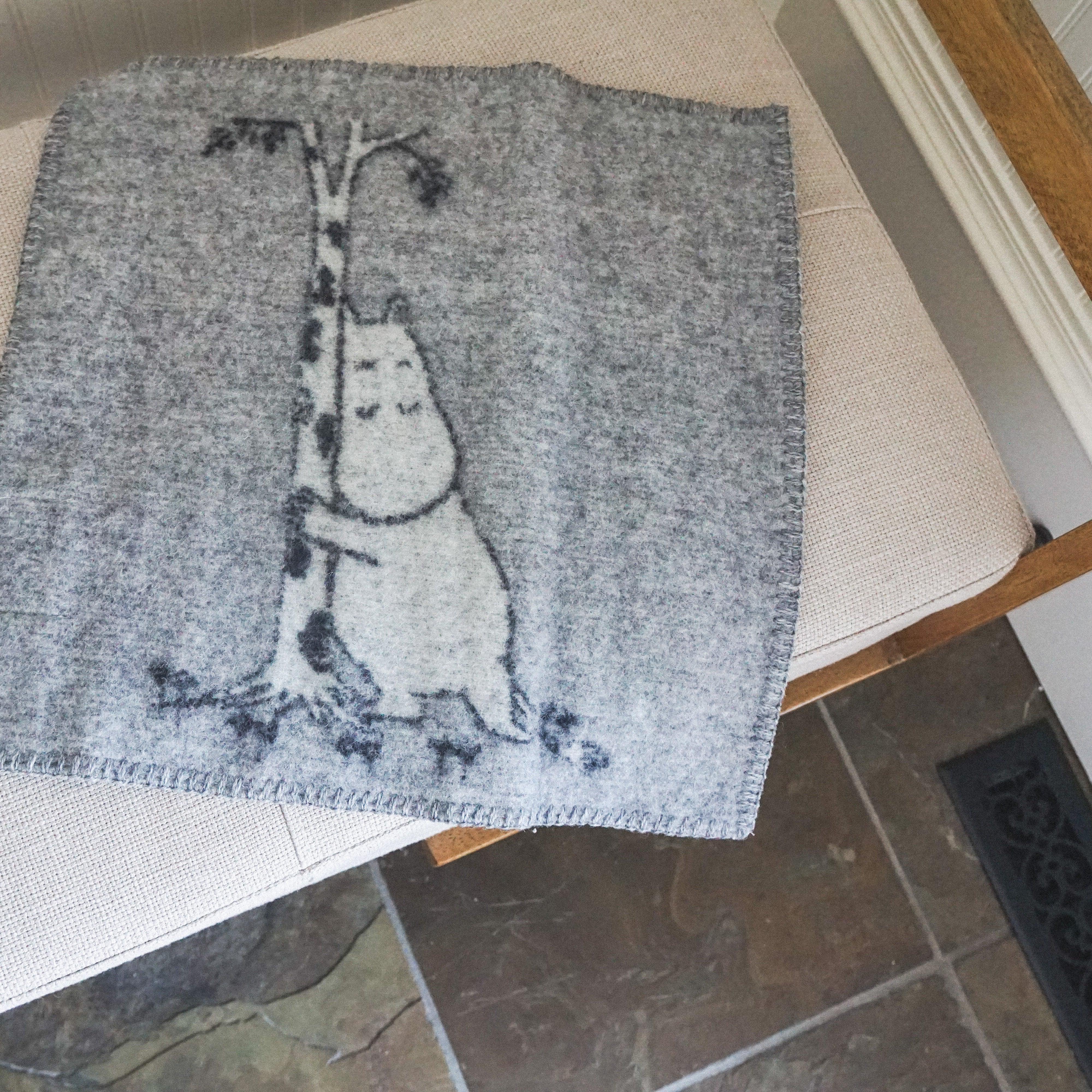 Grace & Company Klippan Lambs Wool Mini Blanket featuring a creature hugging a tree on a beige cushioned bench.
